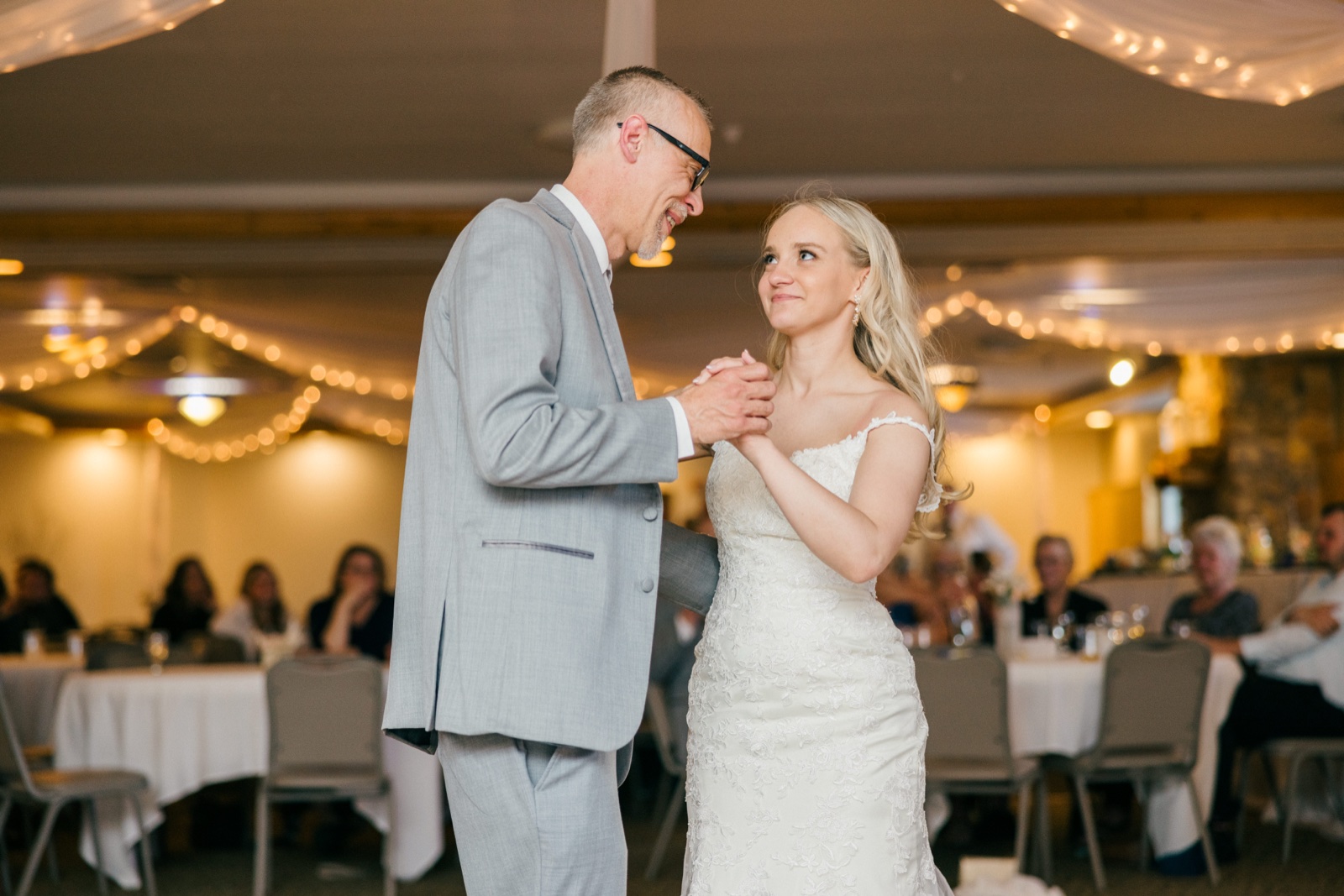 The bride looks up at her father with a small smile as they dance together beneath draped fabric and string lights at the reception — Tim Larsen Photography, Brainerd Lakes MN