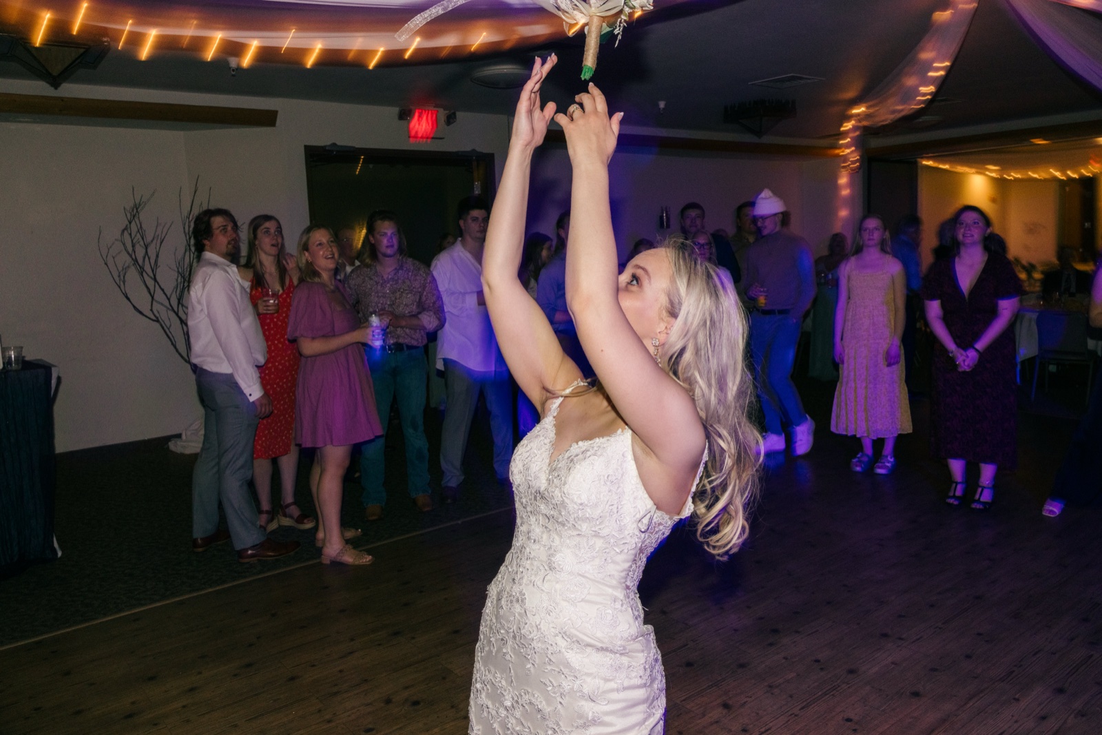 The bride reaches up with both arms as her bouquet flies into the air above the dance floor, with guests watching from the background under string lights — Tim Larsen Photography, Brainerd Lakes MN
