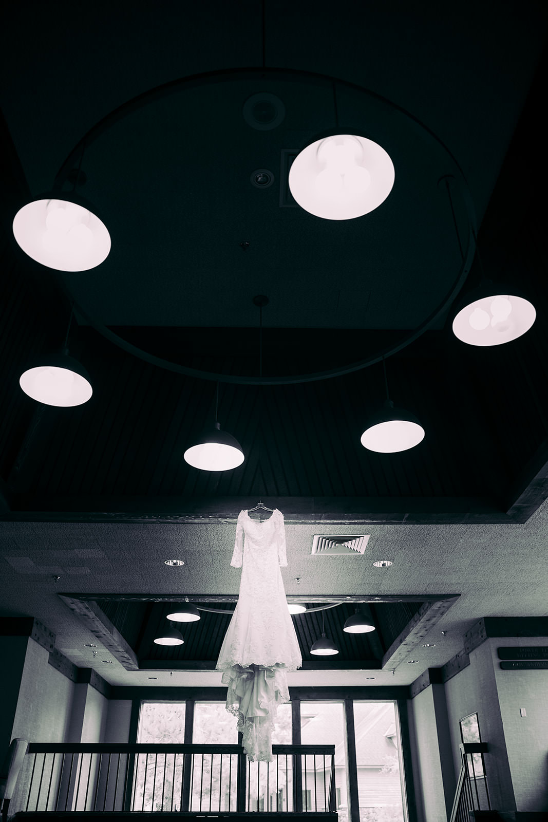 Bride's lace gown hanging from a dramatic circular pendant chandelier in a Madden's on Gull Lake getting-ready space — Tim Larsen Photography, Brainerd Lakes MN