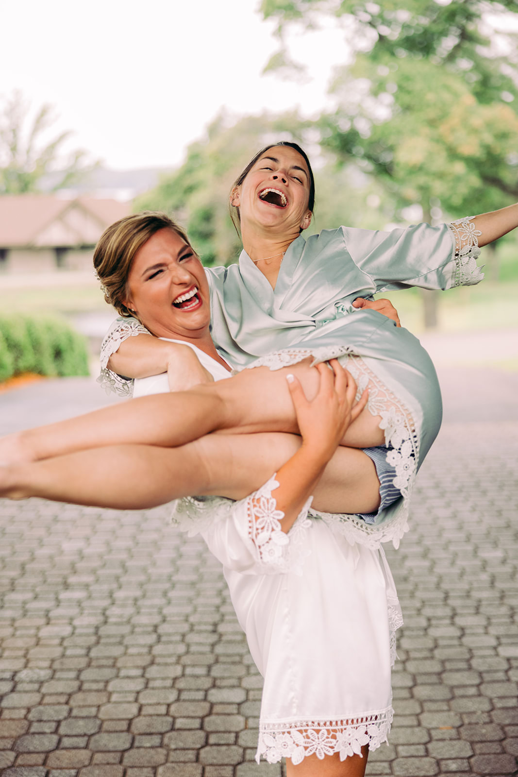 Bride and a bridesmaid laughing in robes — one lifting the other bridal-carry style — Tim Larsen Photography, Brainerd Lakes MN