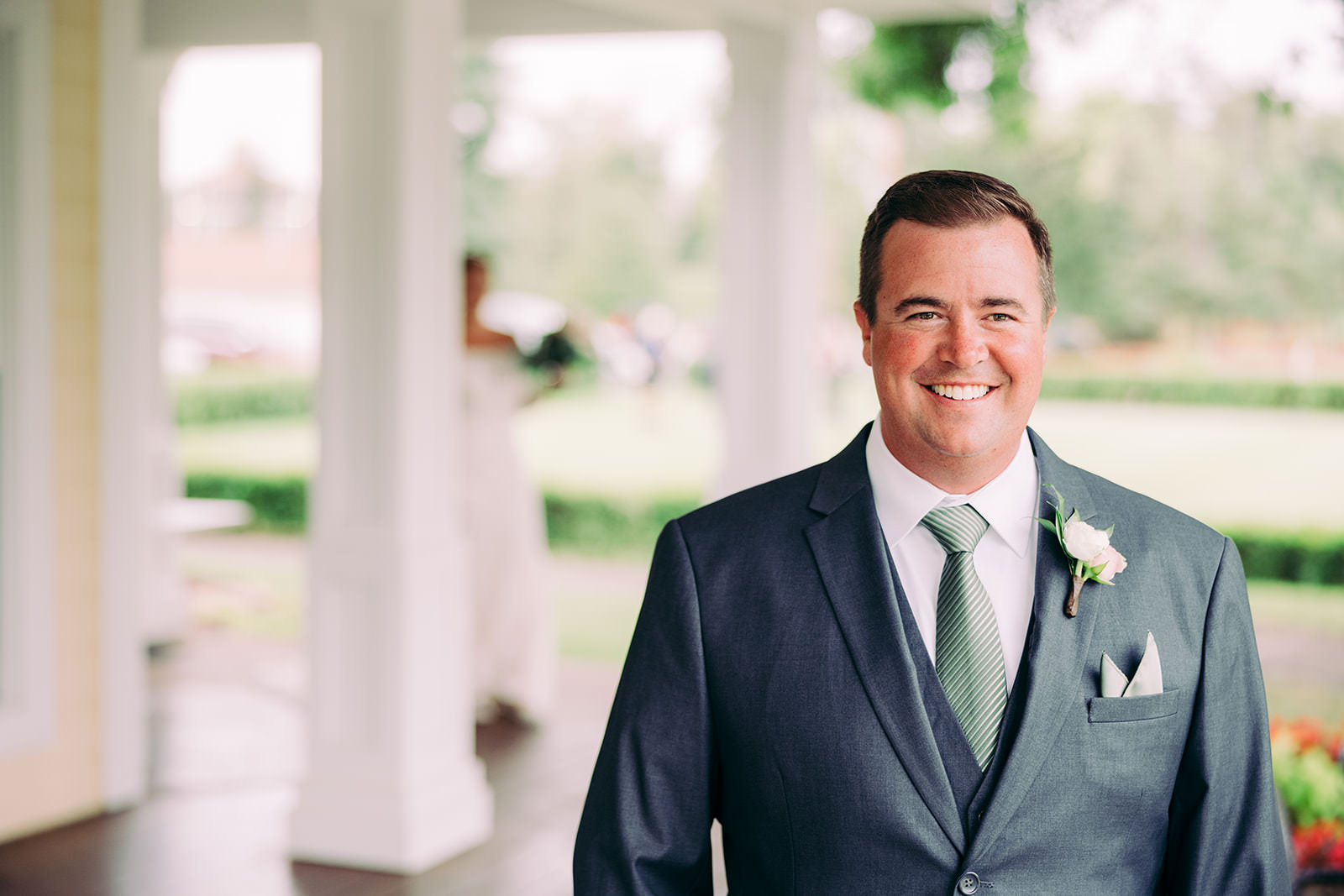 Groom portrait on the Madden's veranda in a charcoal suit with a sage green striped tie and blush rose boutonnière — Tim Larsen Photography, Brainerd Lakes MN