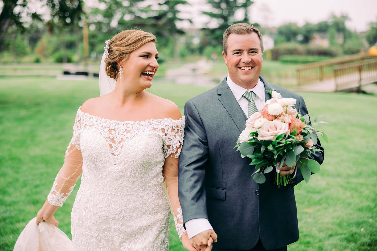 Couple walking hand in hand across a green lawn at Madden's on Gull Lake, groom holding the bouquet — Tim Larsen Photography, Brainerd Lakes MN