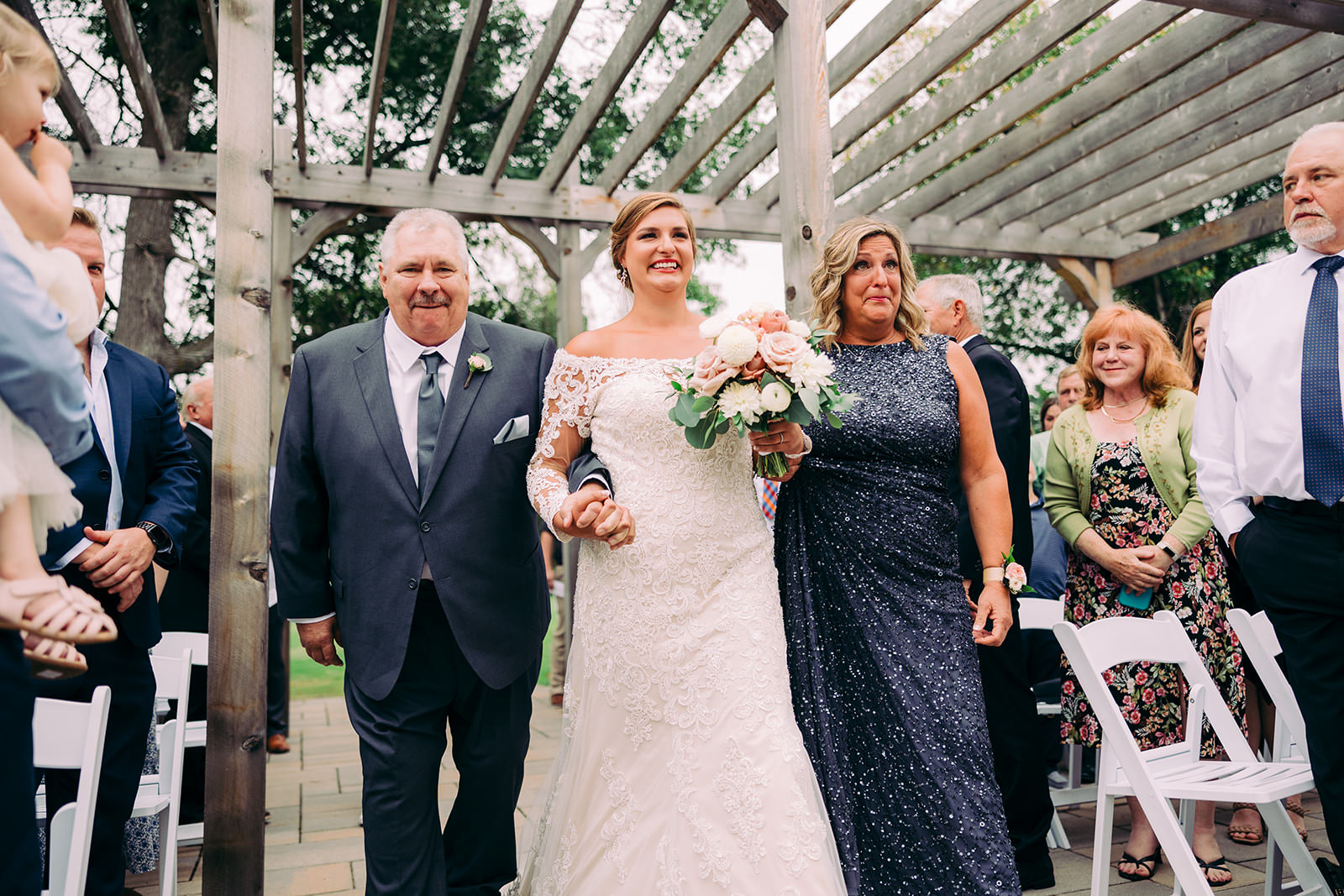 Bride walking down the aisle with both parents under the pergola at Madden's — Tim Larsen Photography, Brainerd Lakes MN