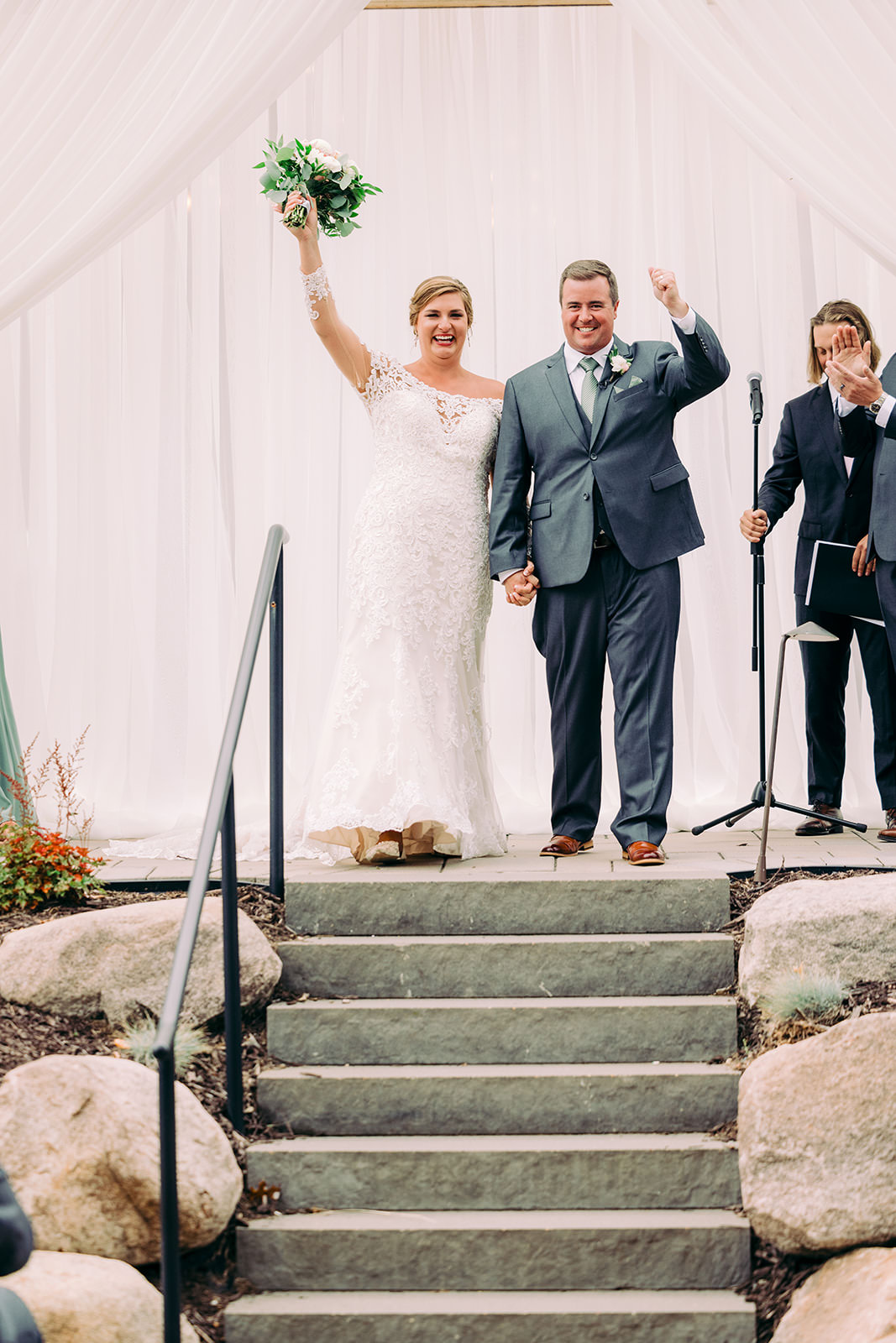 Recessional — couple raising the bouquet as they come back up the stone staircase after the ceremony — Tim Larsen Photography, Brainerd Lakes MN