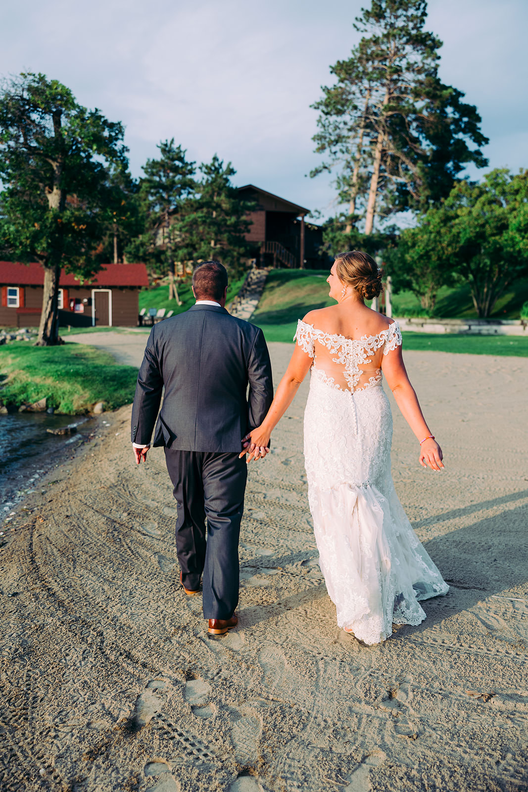 Couple walking away across the sandy Gull Lake shoreline toward the Madden's lodge buildings — Tim Larsen Photography, Brainerd Lakes MN