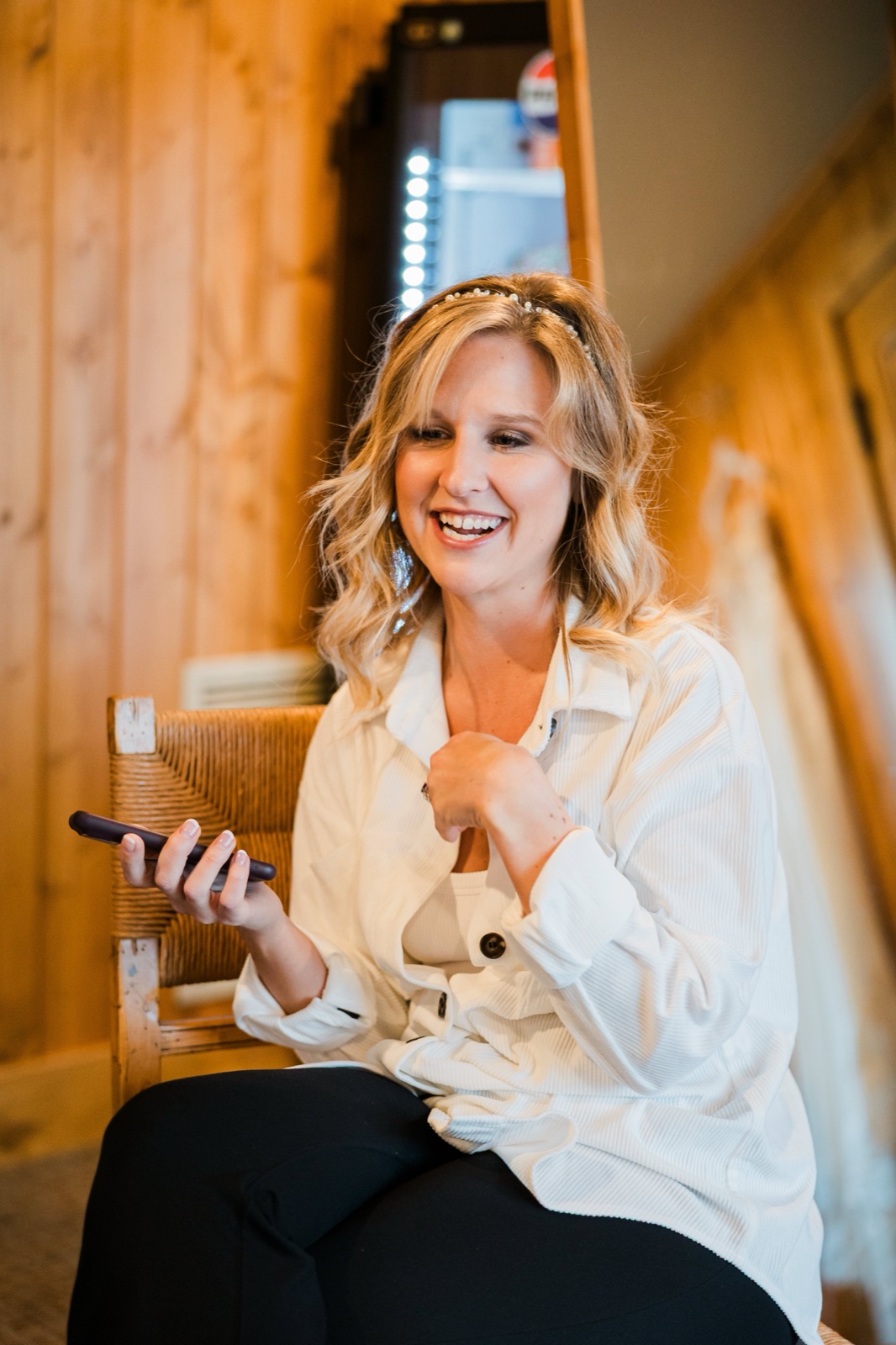 Bride mid-laugh with her phone in hand in a wood-paneled getting-ready room at Madden's