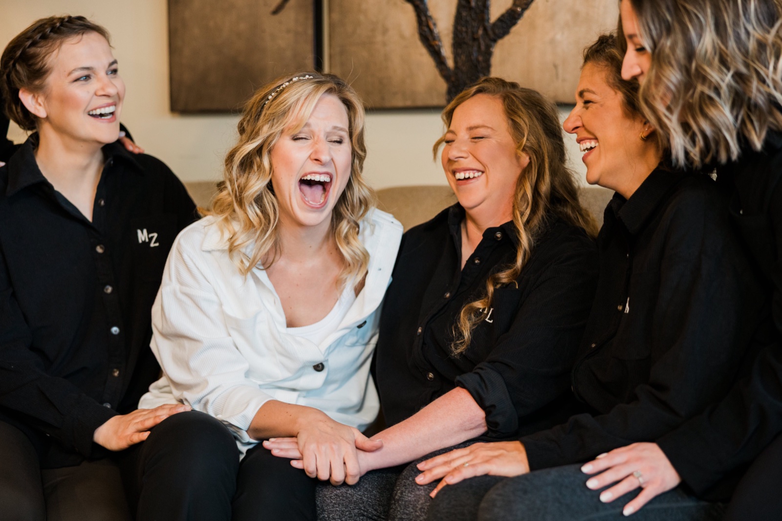 Bride laughing with her bridesmaids on a couch in the getting-ready suite at Madden's on Gull Lake