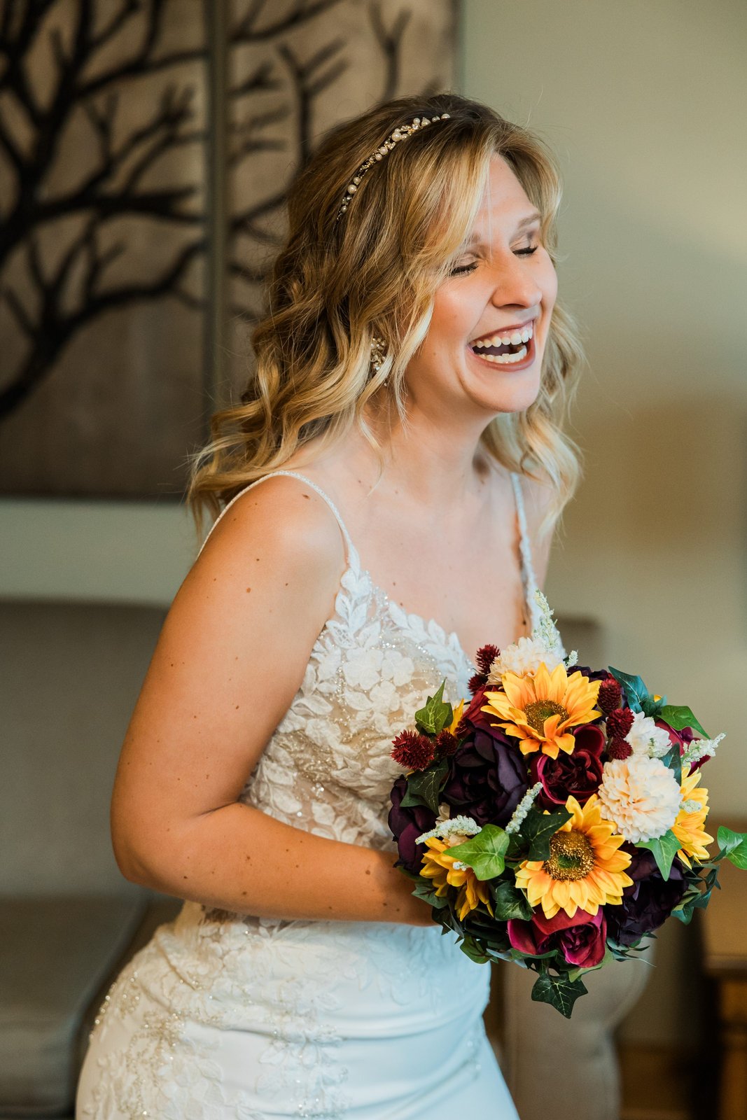 Bride laughing with her sunflower and dahlia bouquet in soft window light at Madden's on Gull Lake