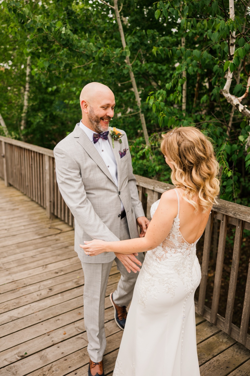 Groom grinning the moment he turns and sees the bride on a wooded boardwalk at Madden's on Gull Lake