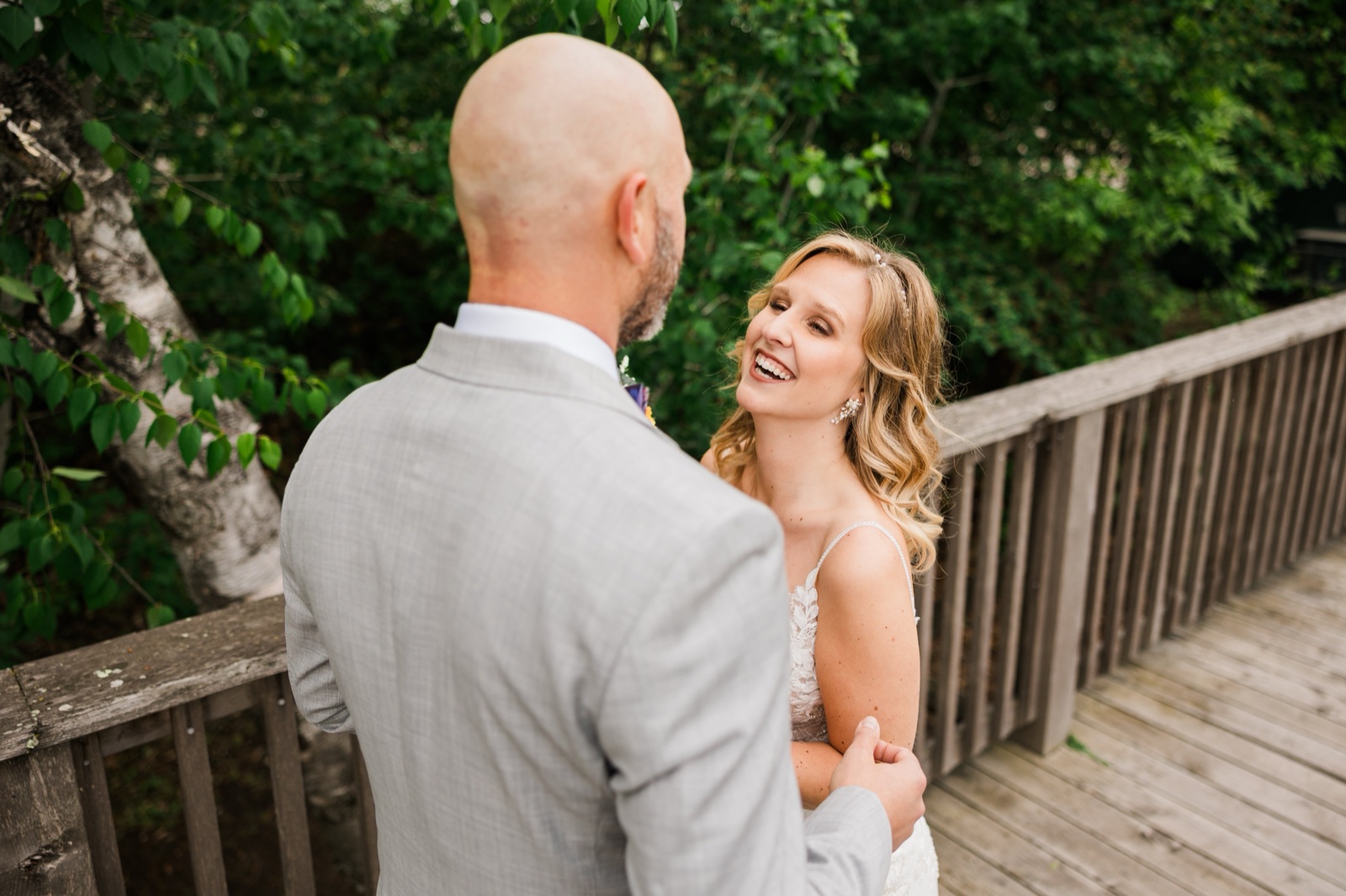 Bride laughing with the groom on a wooden footbridge framed by green spring foliage at Madden's
