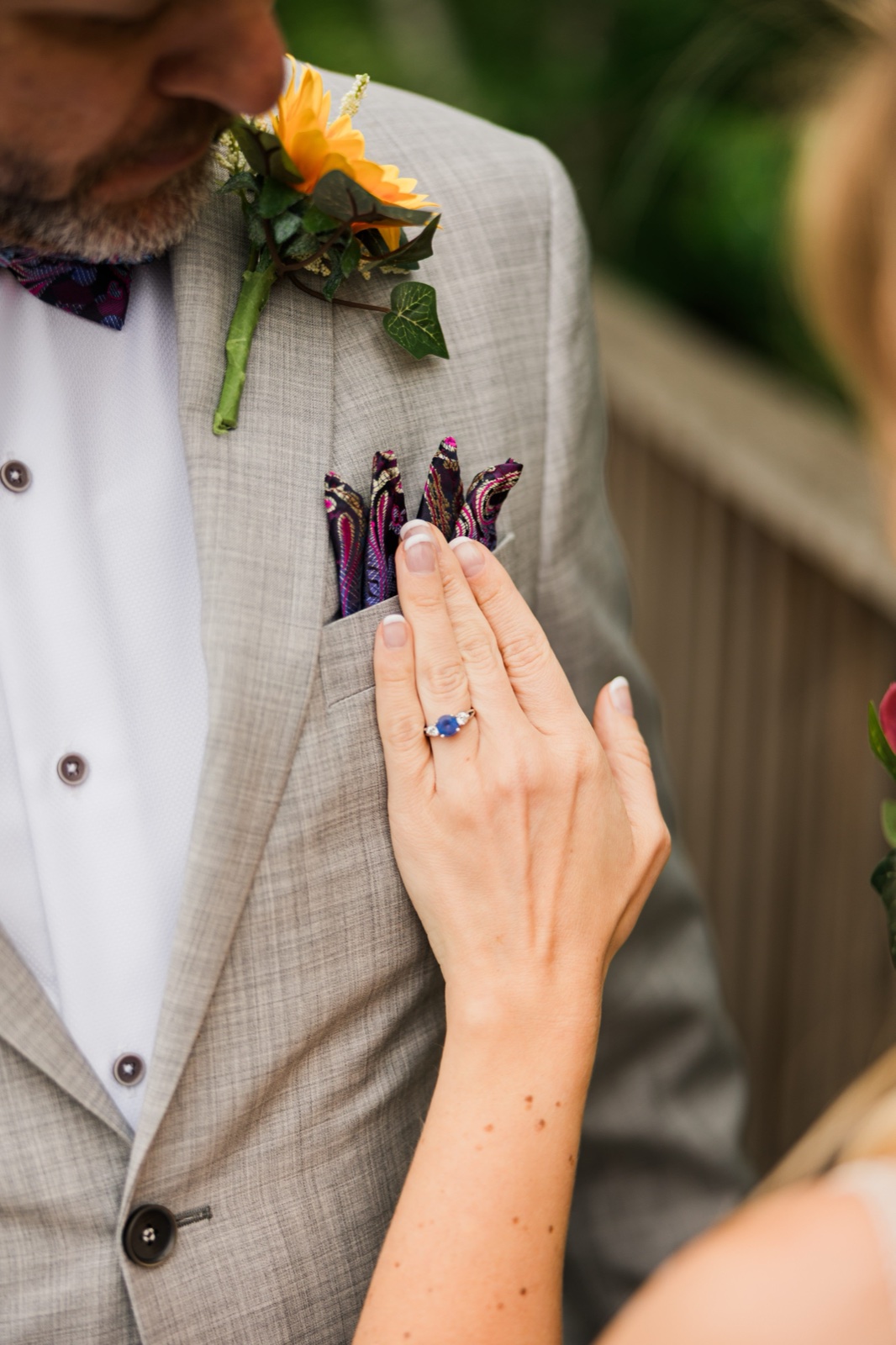 Bride's sapphire ring resting on the groom's lapel next to his sunflower boutonniere and paisley pocket square