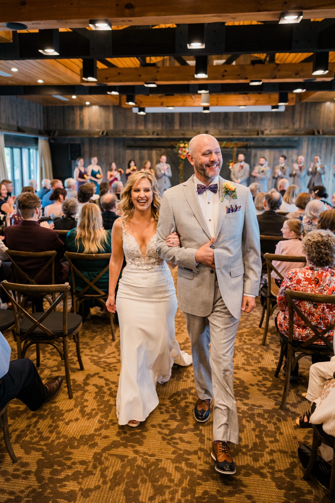 Bride and groom laughing through the recessional as guests cheer under the wood-beamed ceiling