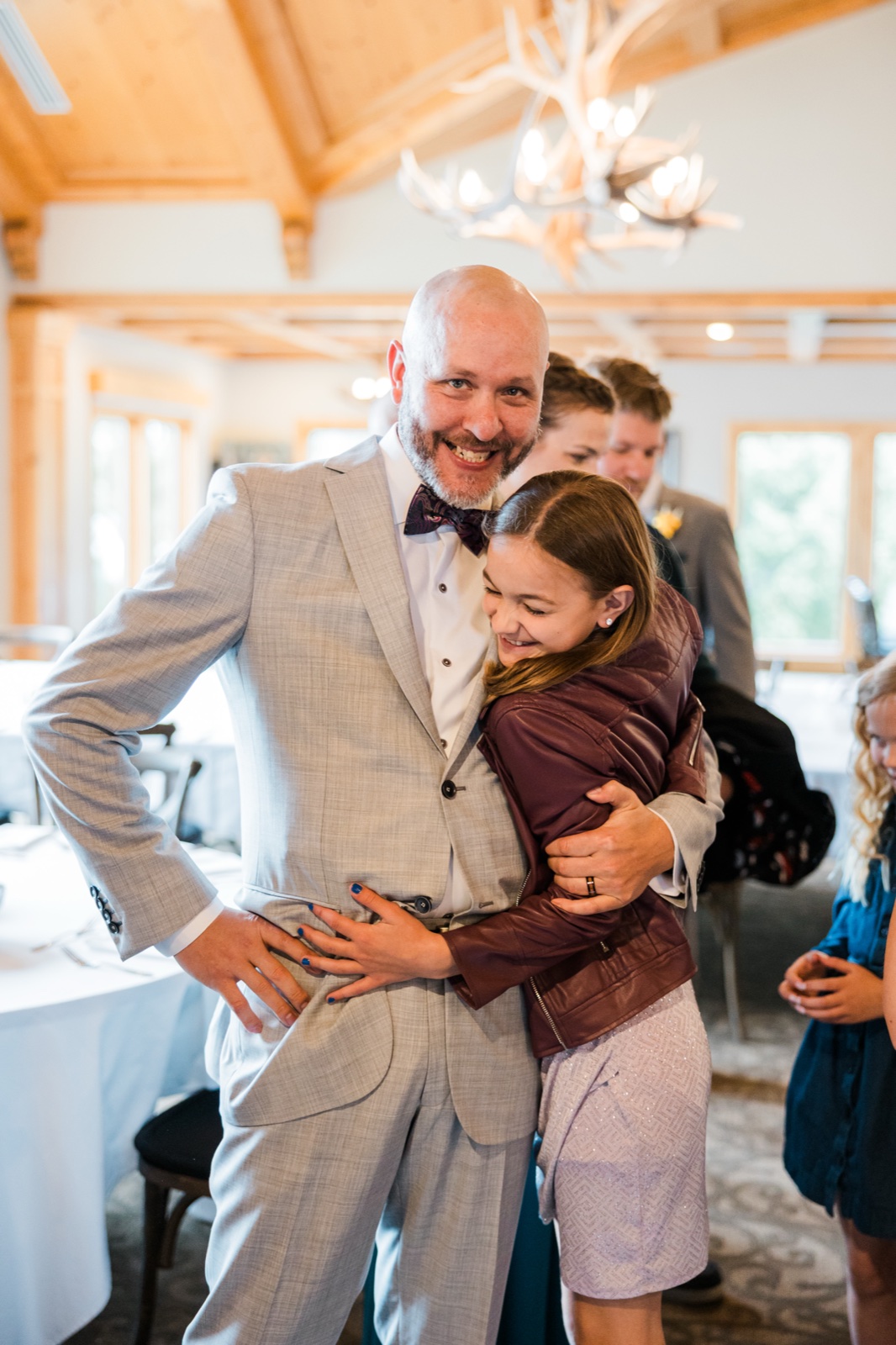 Young niece in a maroon jacket hugging a guest under the antler chandelier in the Madden's reception hall