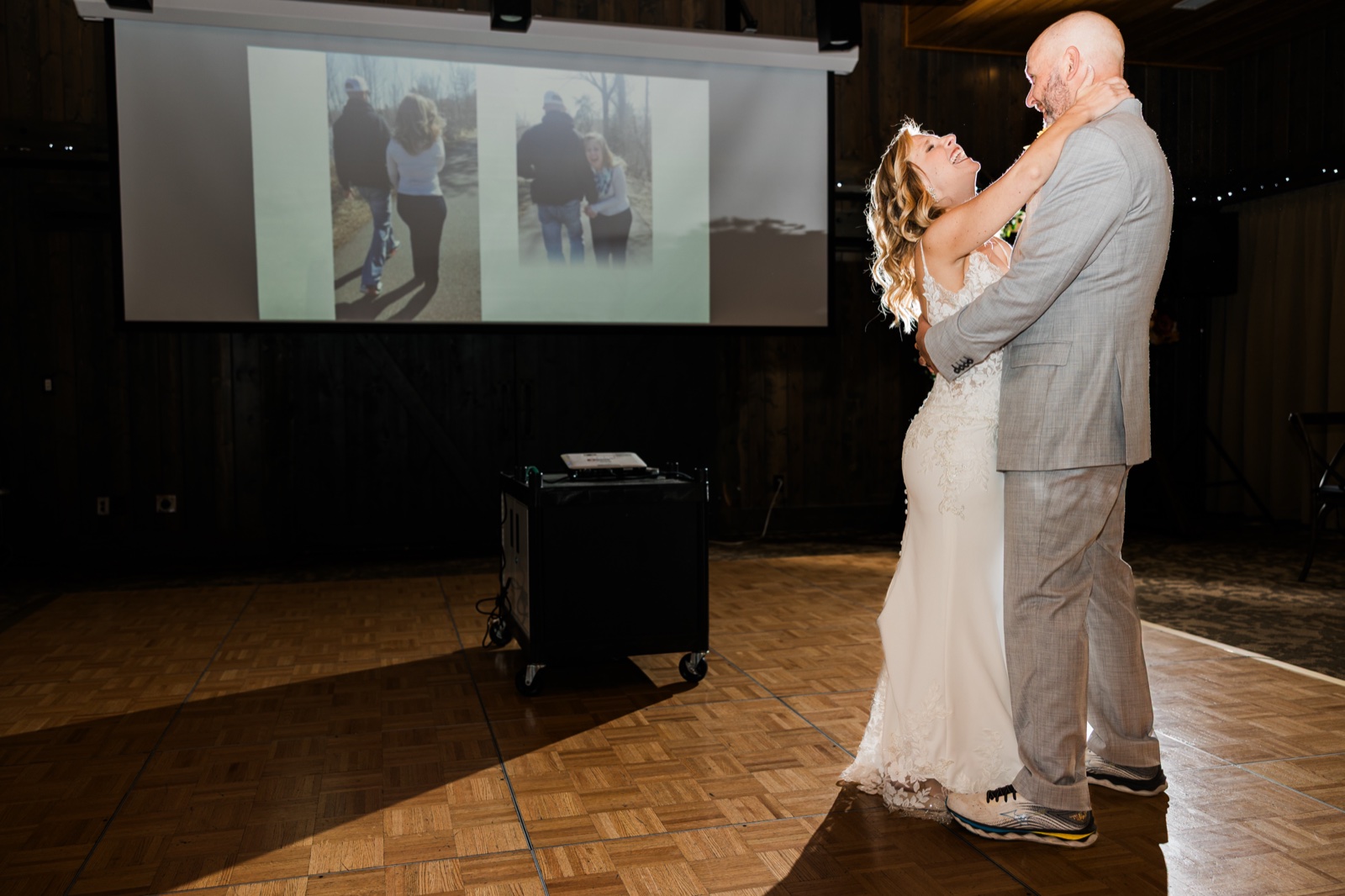 Bride laughing during her father-daughter dance as a slideshow of childhood photos plays behind them