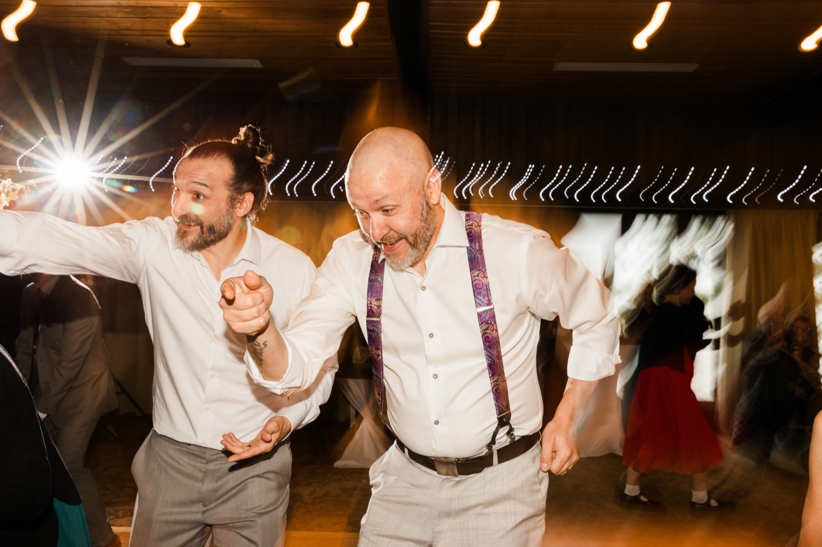 Two guests in paisley suspenders grinning on a packed dance floor under string lights at Madden's