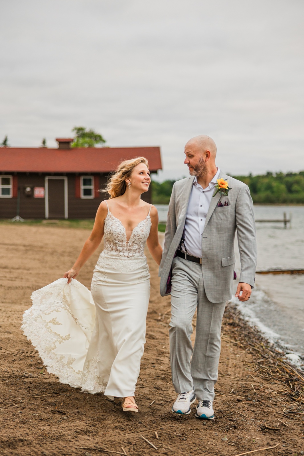Bride and groom walking the sandy Gull Lake shoreline at Madden's, lace train behind her