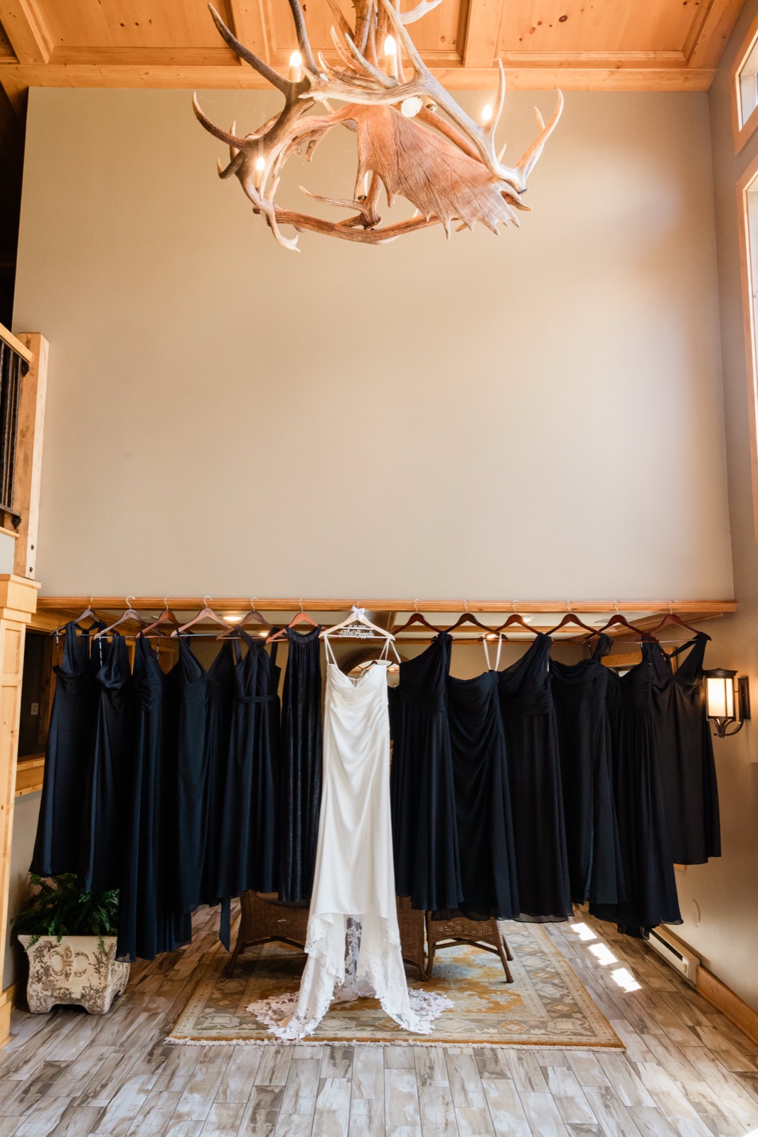The bride's white gown hanging at center among a row of navy bridesmaid dresses beneath a large antler chandelier in a wood-paneled Madden's cabin — Tim Larsen Photography, Brainerd Lakes MN