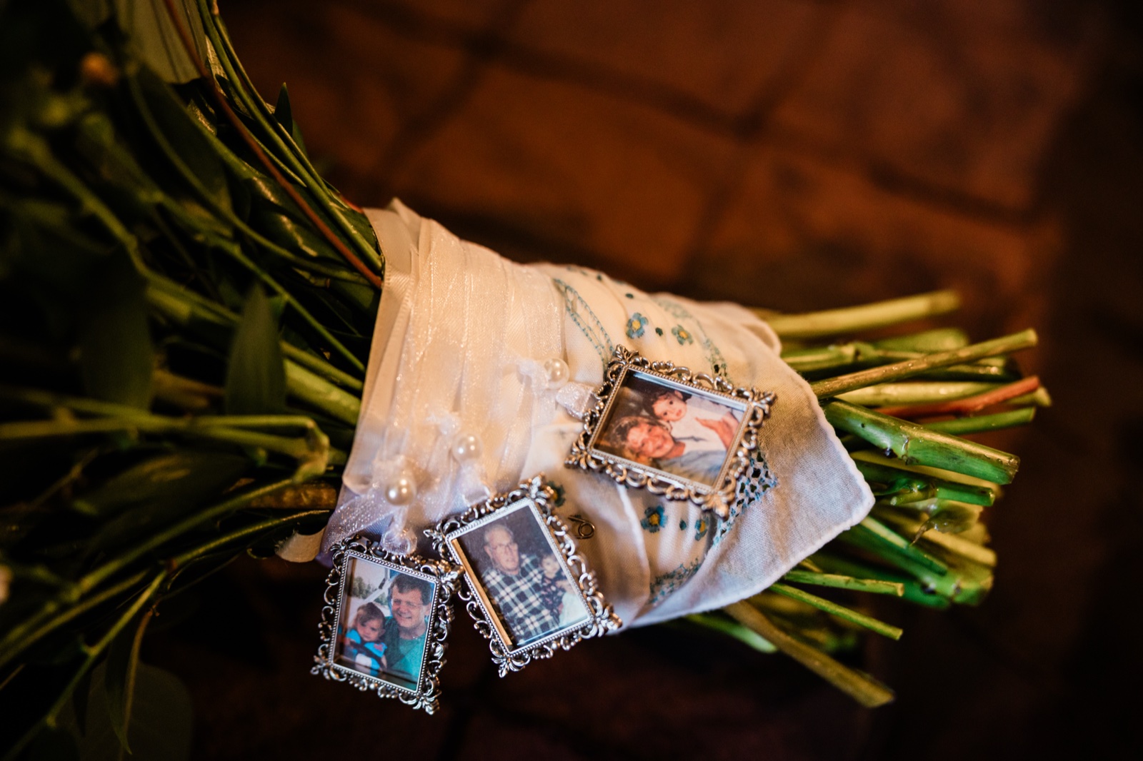 Three ornate silver-framed memorial photographs tucked into the ribbon wrap of the bride's bouquet over an embroidered handkerchief — Tim Larsen Photography, Brainerd Lakes MN