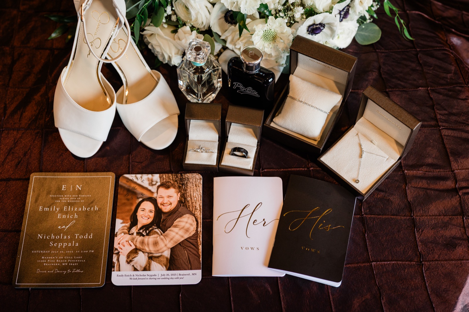 Overhead lay-flat of ivory heels, white bouquet, perfume bottles, wedding rings, a save-the-date, and his-and-her vow books on a textured quilted surface — Tim Larsen Photography, Brainerd Lakes MN