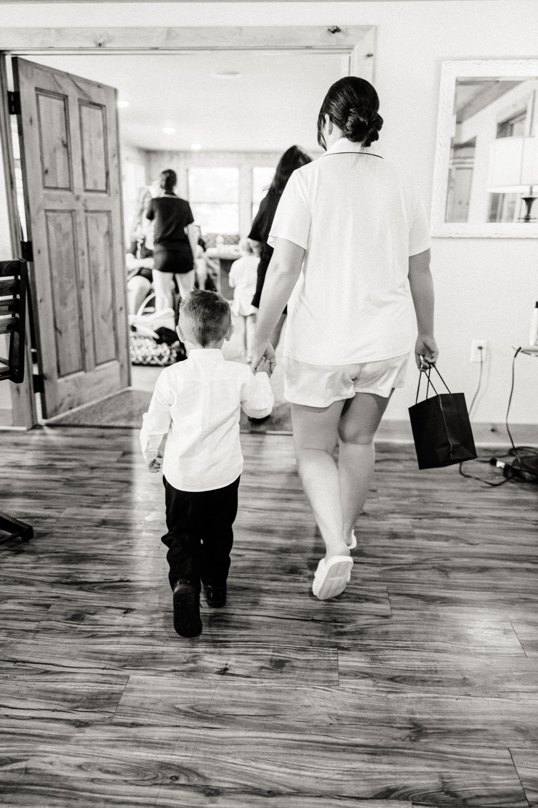 A woman in pajamas walking away hand-in-hand with a small ring bearer through a doorway into the getting-ready room — Tim Larsen Photography, Brainerd Lakes MN