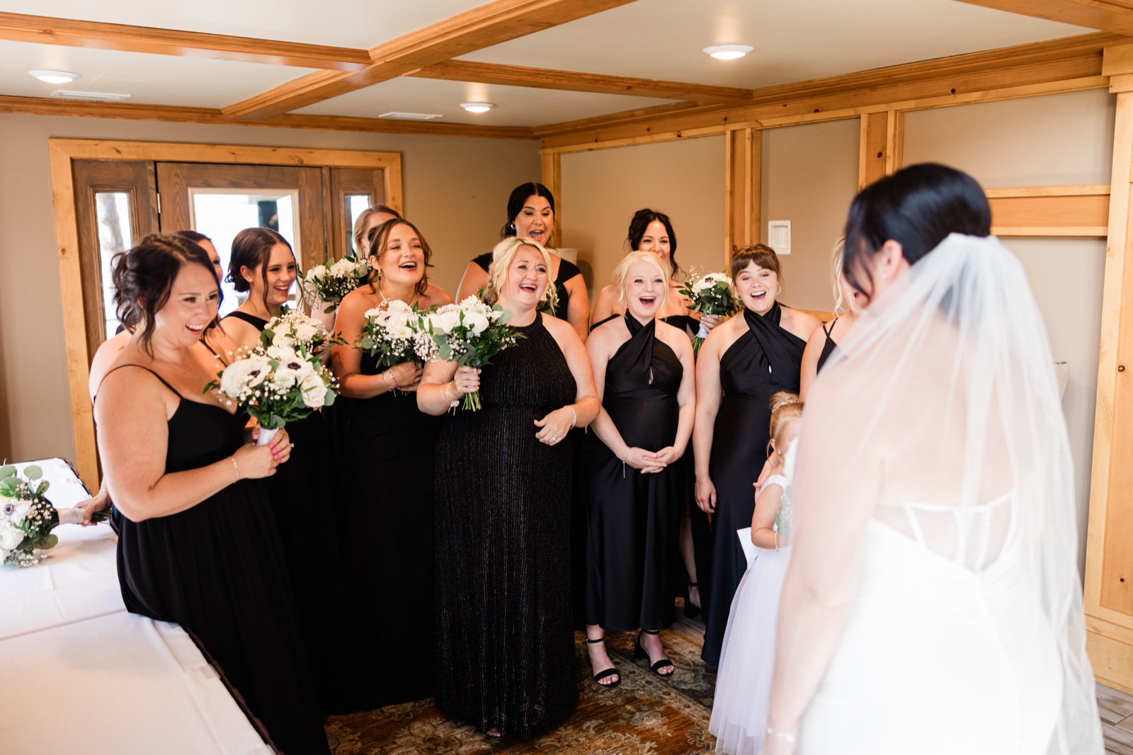 Bridesmaids in black dresses laughing and gasping as they see the bride in her veil for the first time — Tim Larsen Photography, Brainerd Lakes MN
