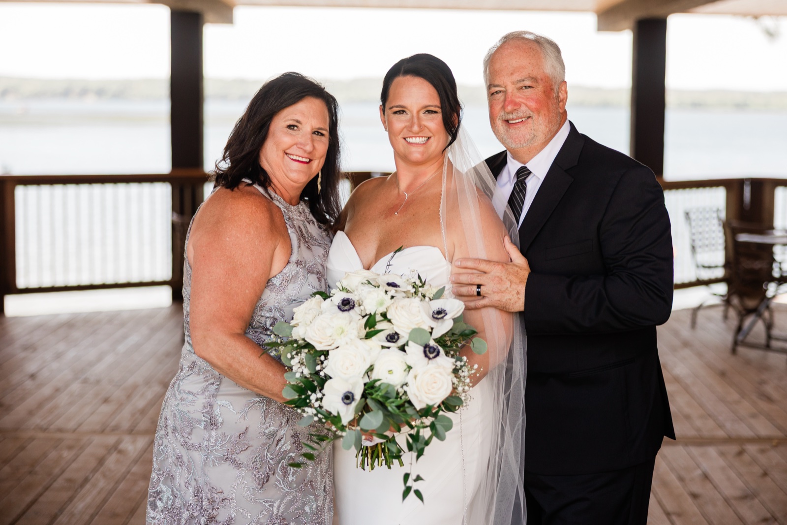 The bride standing between her parents in the covered Madden's Pavilion with Gull Lake visible behind them — Tim Larsen Photography, Brainerd Lakes MN
