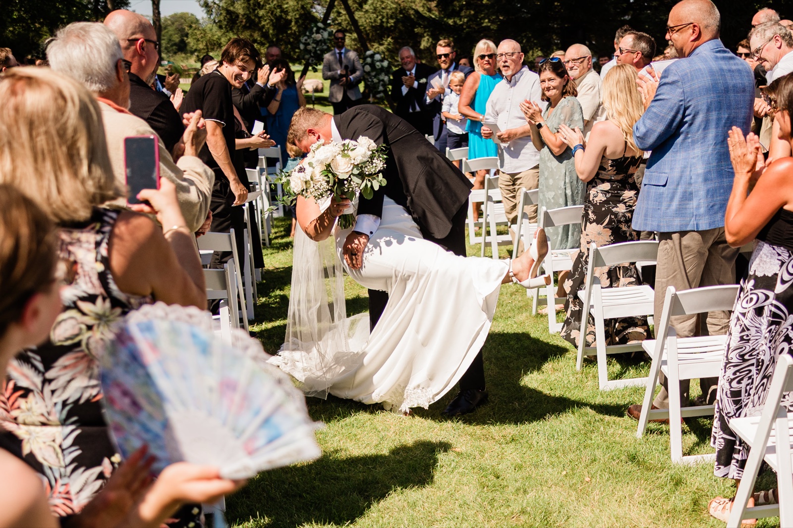 The groom dipping the bride for a kiss halfway down the aisle as guests stand and applaud after the ceremony — Tim Larsen Photography, Brainerd Lakes MN