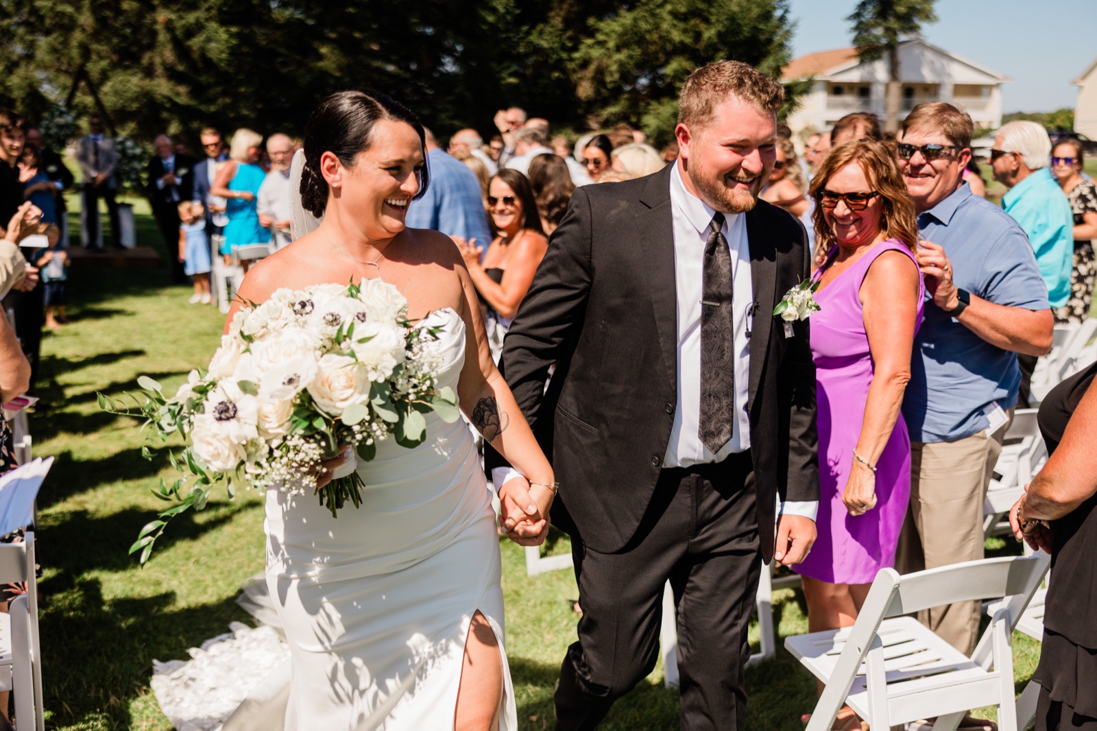 The bride and groom walking hand-in-hand down the outdoor aisle after the ceremony, both laughing, guests cheering on either side — Tim Larsen Photography, Brainerd Lakes MN