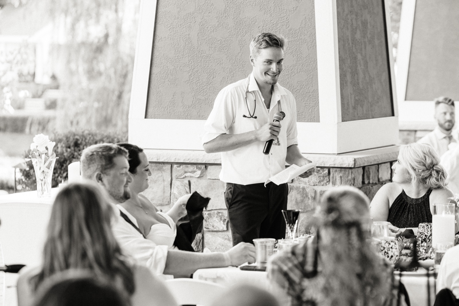 A groomsman in an open white shirt and stethoscope grinning during a toast on the Madden's Pavilion reception floor — Tim Larsen Photography, Brainerd Lakes MN