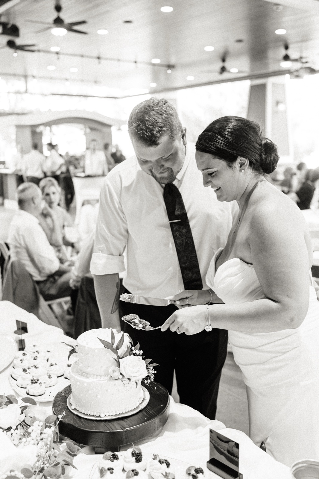 The bride and groom lean in together to lift the first slice from their two-tier floral-topped cake at Madden's — Tim Larsen Photography, Brainerd Lakes MN