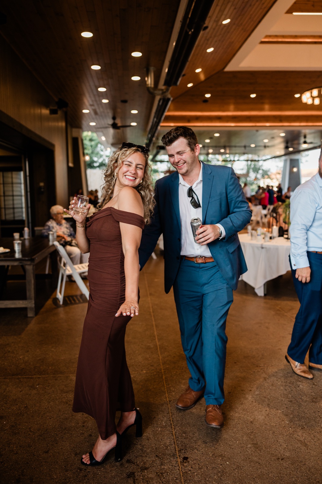 Two guests laugh together holding drinks under the wood-beamed ceiling of the Madden's Pavilion at cocktail hour — Tim Larsen Photography, Brainerd Lakes MN