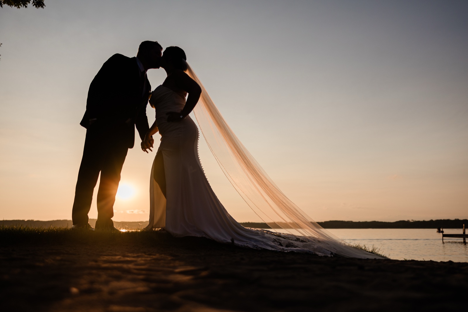 Silhouetted kiss on the Madden's lakeshore at sunset, the bride's veil stretched across the sand toward Gull Lake — Tim Larsen Photography, Brainerd Lakes MN