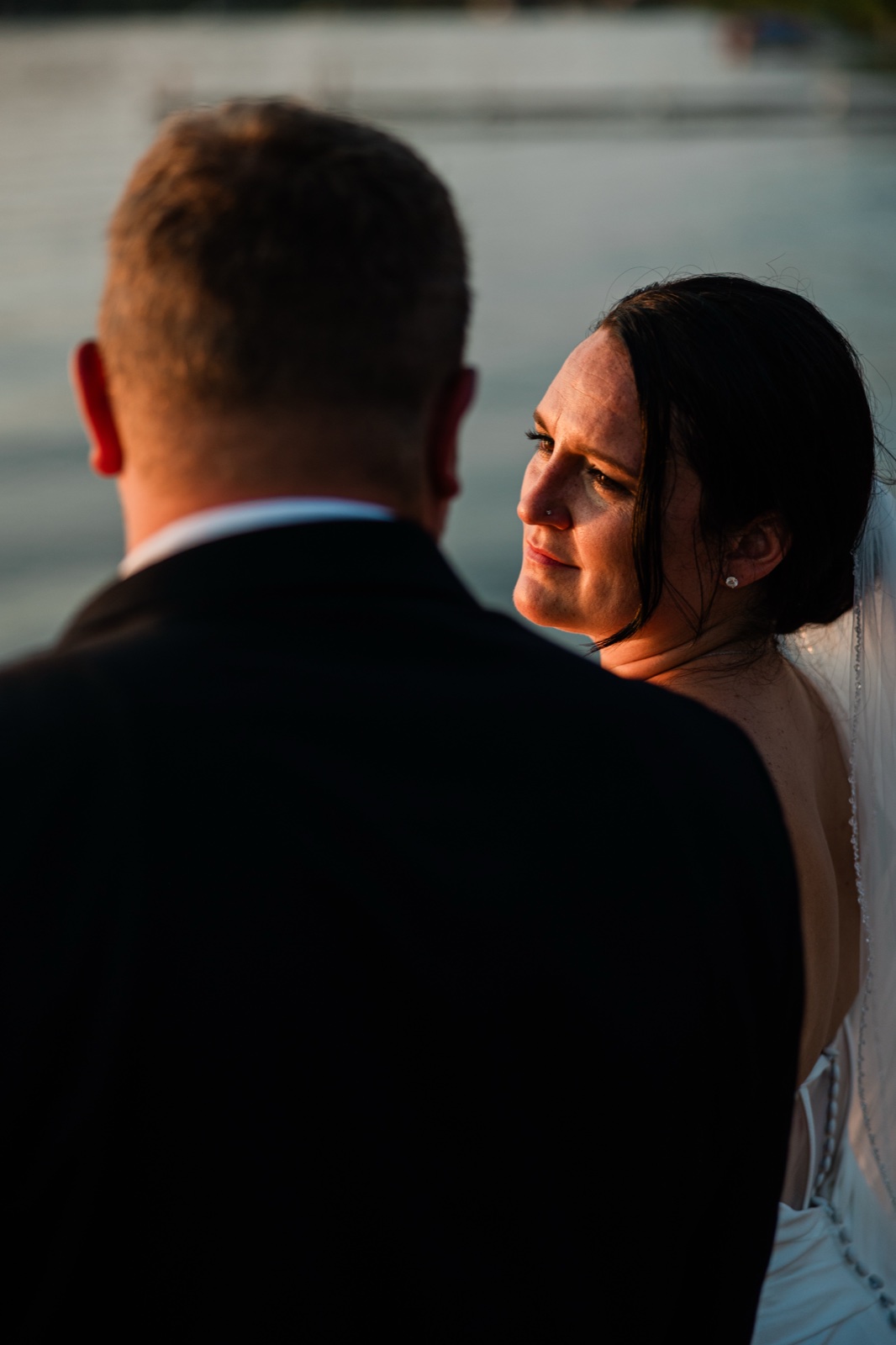 Warm evening light on the bride's face as she holds her groom's look by the cool blue water of Gull Lake behind them — Tim Larsen Photography, Brainerd Lakes MN