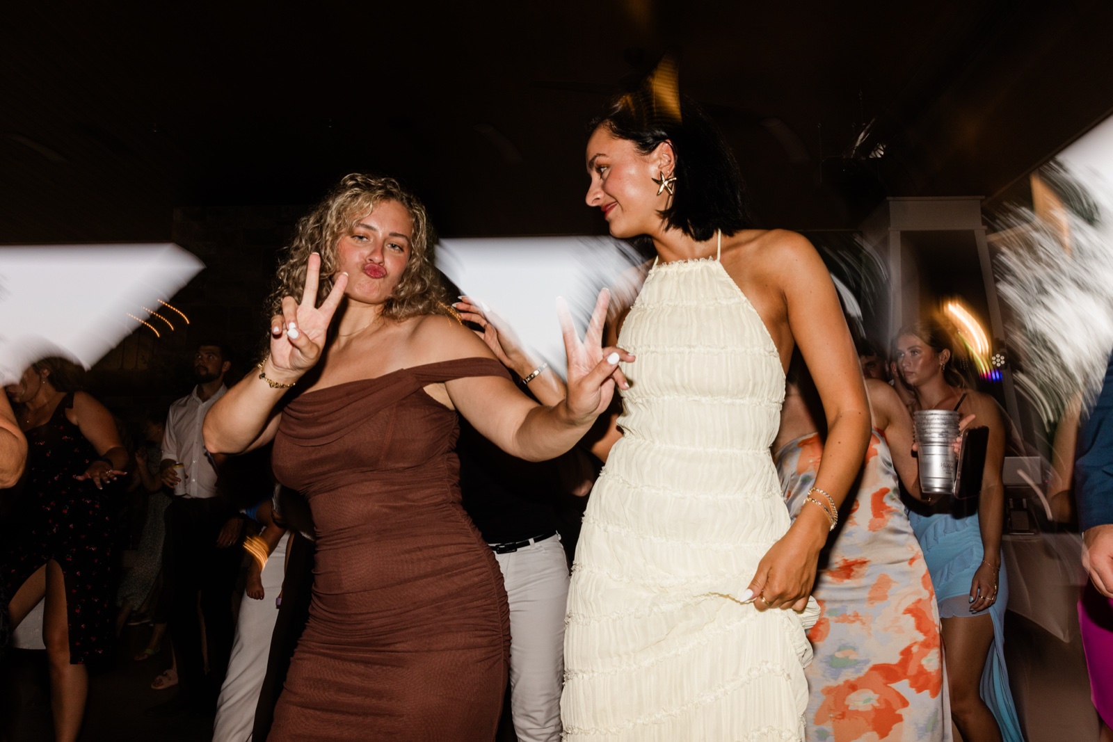 Two guests in brown and cream dresses pose playfully on the Madden's dance floor as light streaks blur behind them — Tim Larsen Photography, Brainerd Lakes MN
