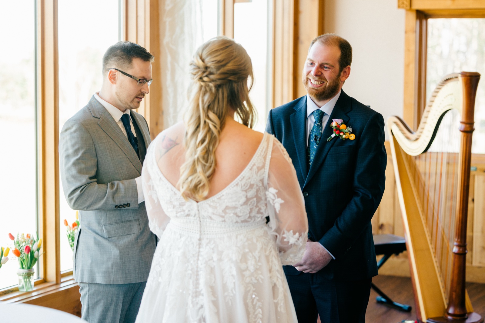 The groom smiles at his bride during the ceremony at Cragun's as the officiant reads beside them in window light — Tim Larsen Photography, Brainerd Lakes MN