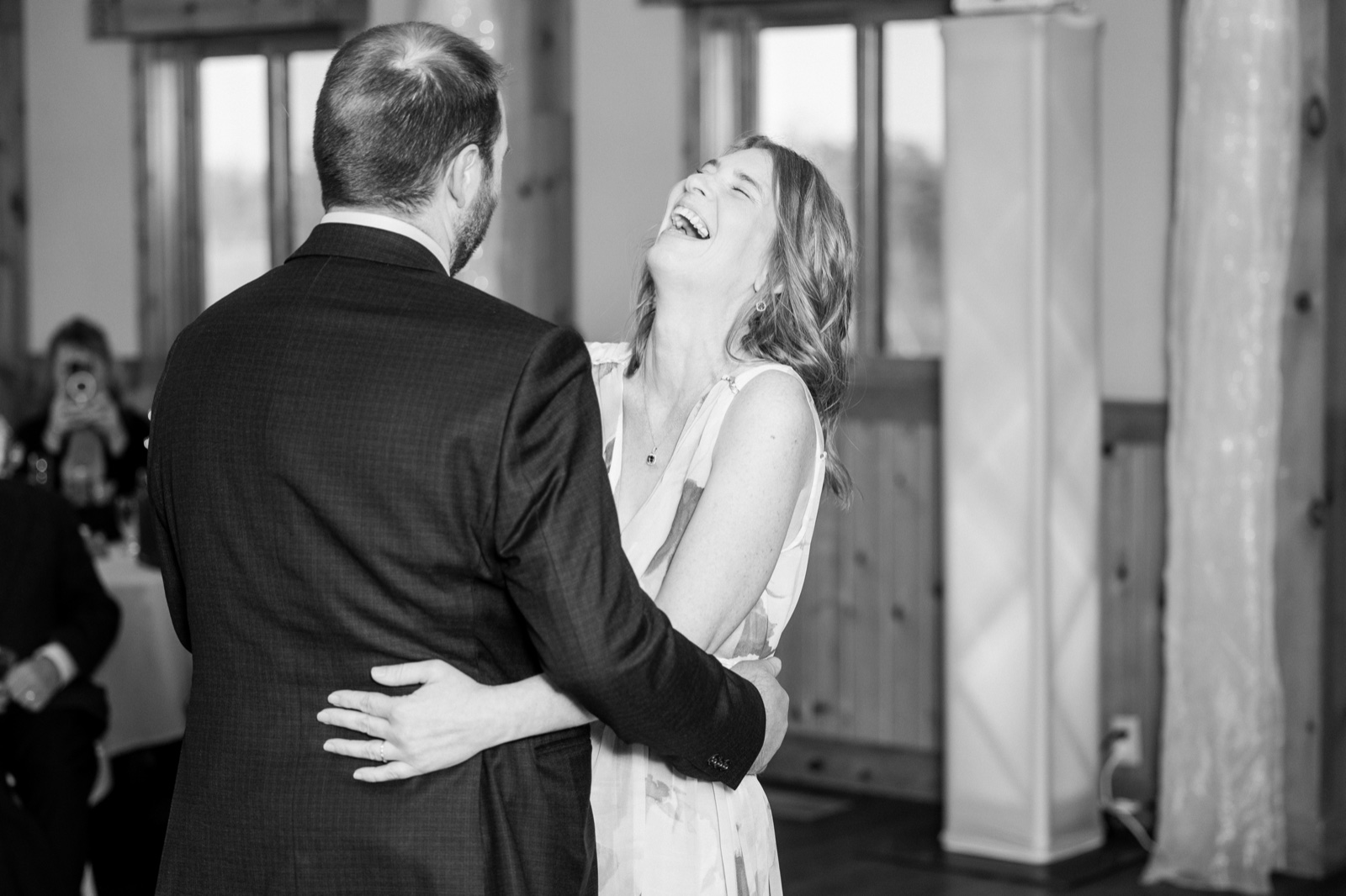 The bride throws her head back in full laughter while embracing the groom in a window-lit reception room at Cragun's Resort — Tim Larsen Photography, Brainerd Lakes MN