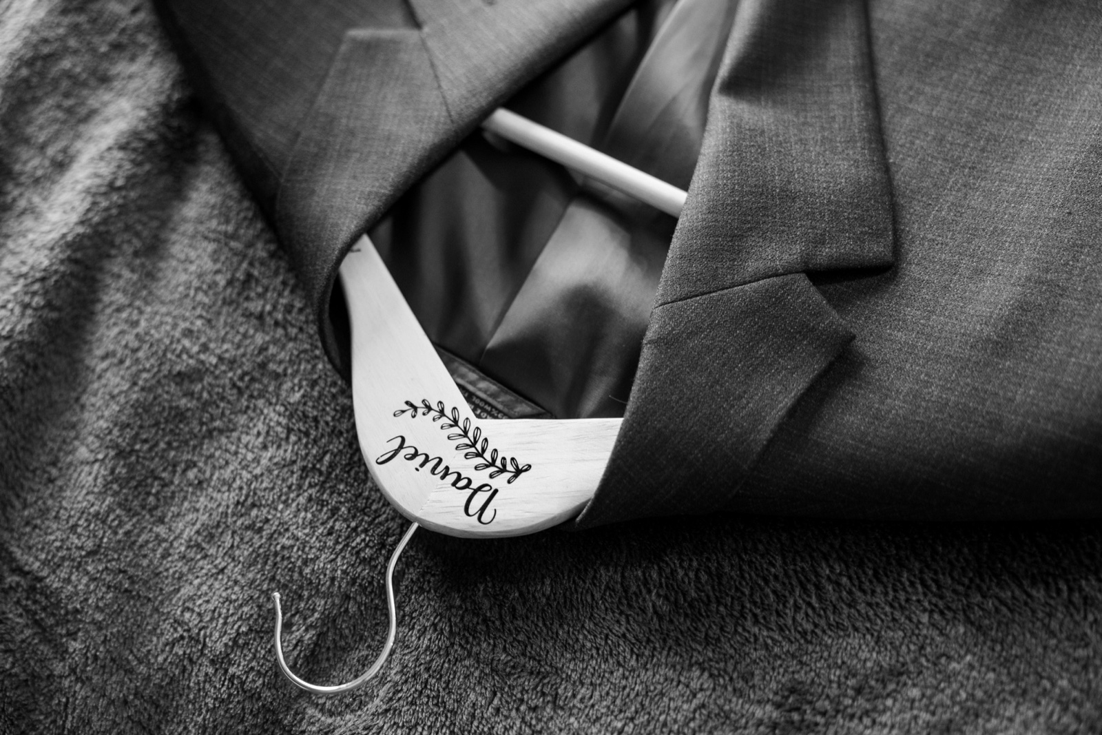 A personalized wooden hanger engraved 'Daniel' resting inside the groom's gray suit jacket on the morning of his Cragun's wedding — Tim Larsen Photography, Brainerd Lakes MN