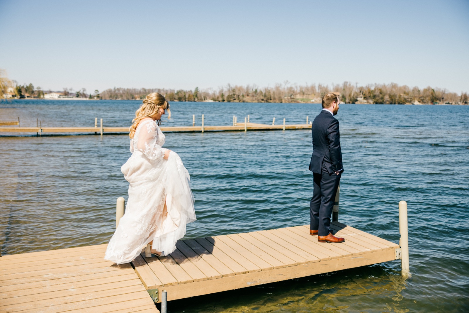The bride lifts her dress as she walks down a wooden dock toward the groom for their first look at Cragun's Resort — Tim Larsen Photography, Brainerd Lakes MN