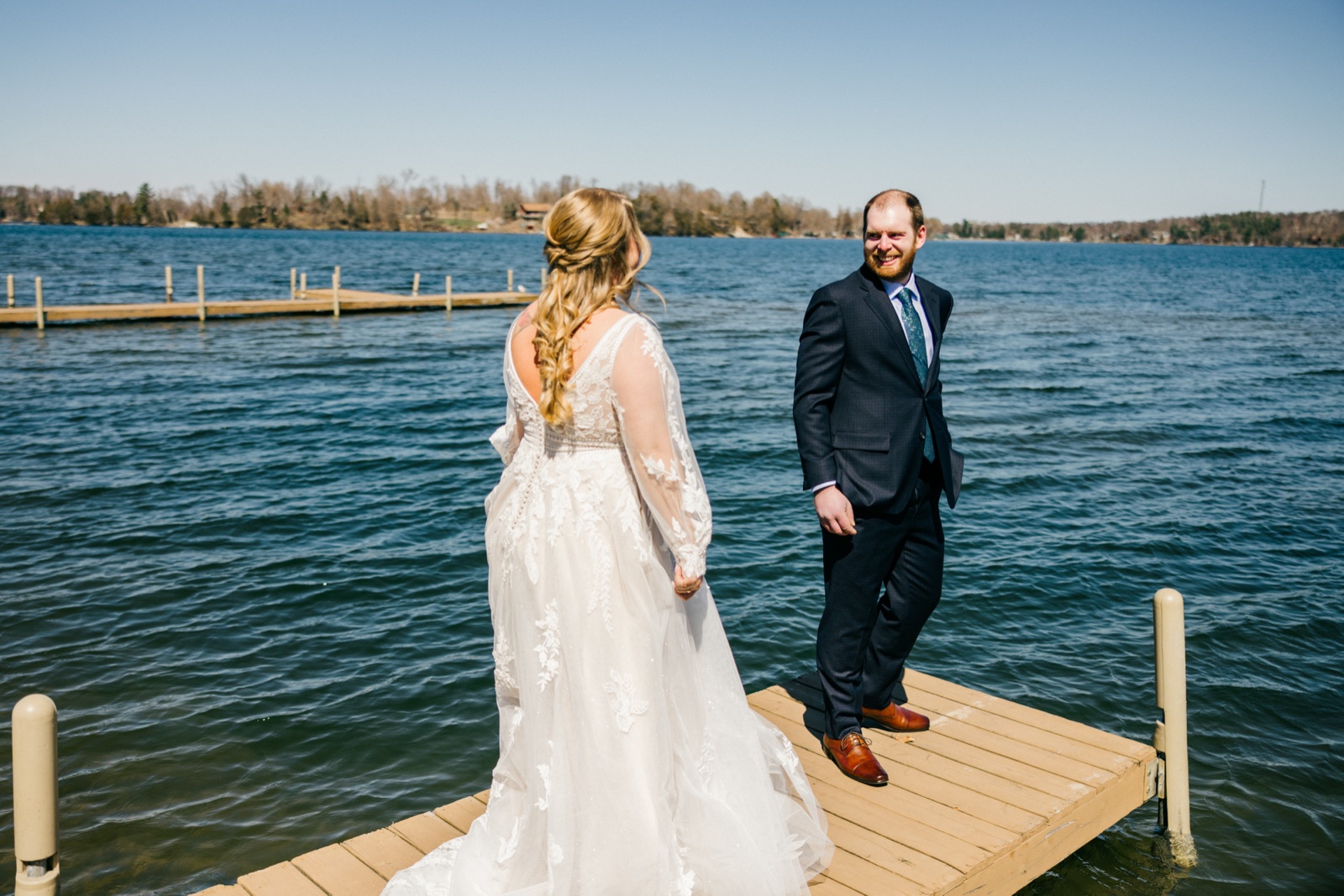 The groom grins at the bride during the first look at the end of the Cragun's dock, Gull Lake stretching out blue behind them — Tim Larsen Photography, Brainerd Lakes MN