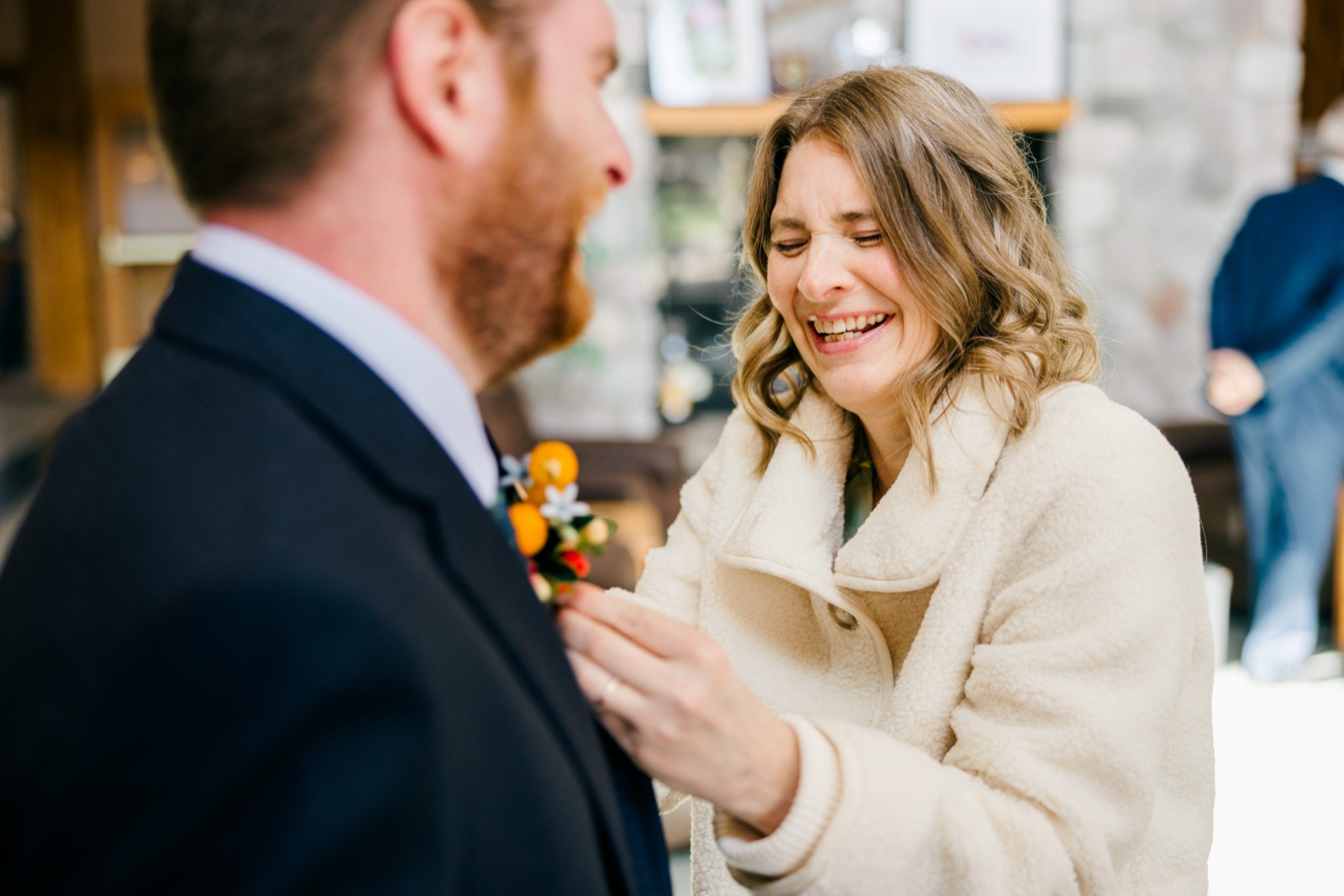 The bride laughs joyfully as she pins a citrus-and-floral boutonniere onto the groom's lapel — Tim Larsen Photography, Brainerd Lakes MN — Tim Larsen Photography, Brainerd Lakes MN