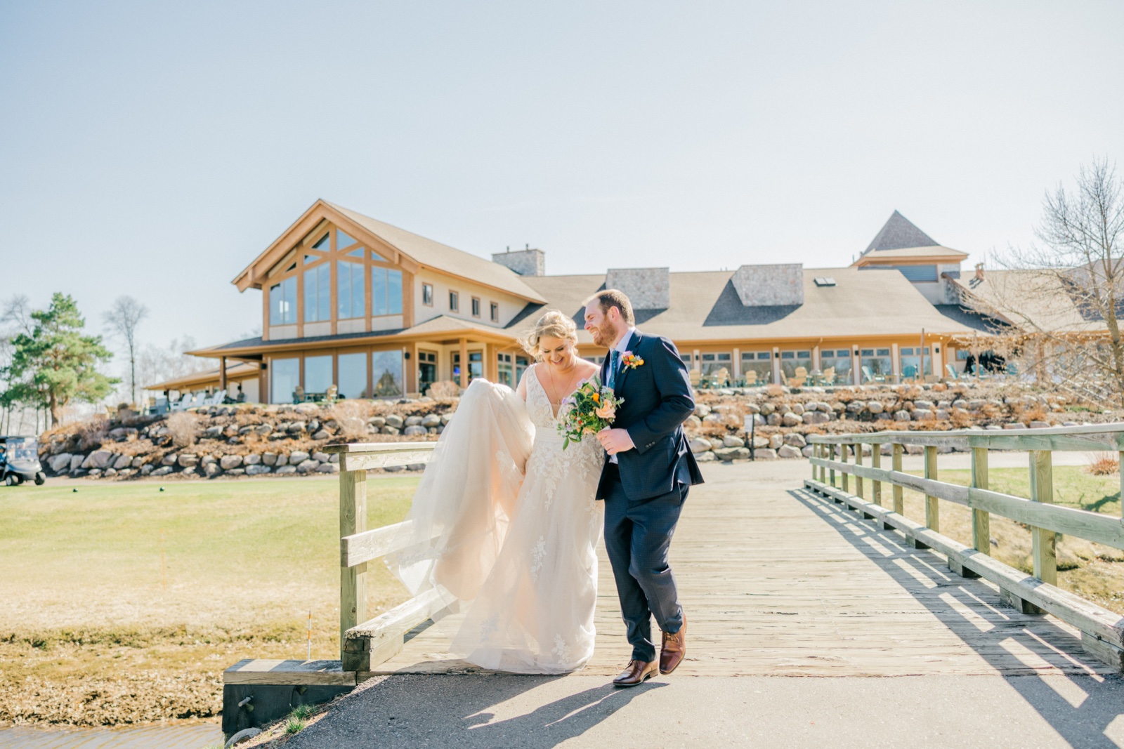 The bride and groom walk together across a wooden bridge with the timber-framed Cragun's Resort lodge filling the background — Tim Larsen Photography, Brainerd Lakes MN