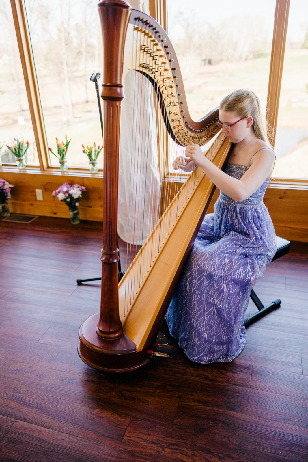 A young harpist in a lavender gown plays a tall pedal harp beside large windows in the wood-paneled ceremony space at Cragun's Resort — Tim Larsen Photography, Brainerd Lakes MN
