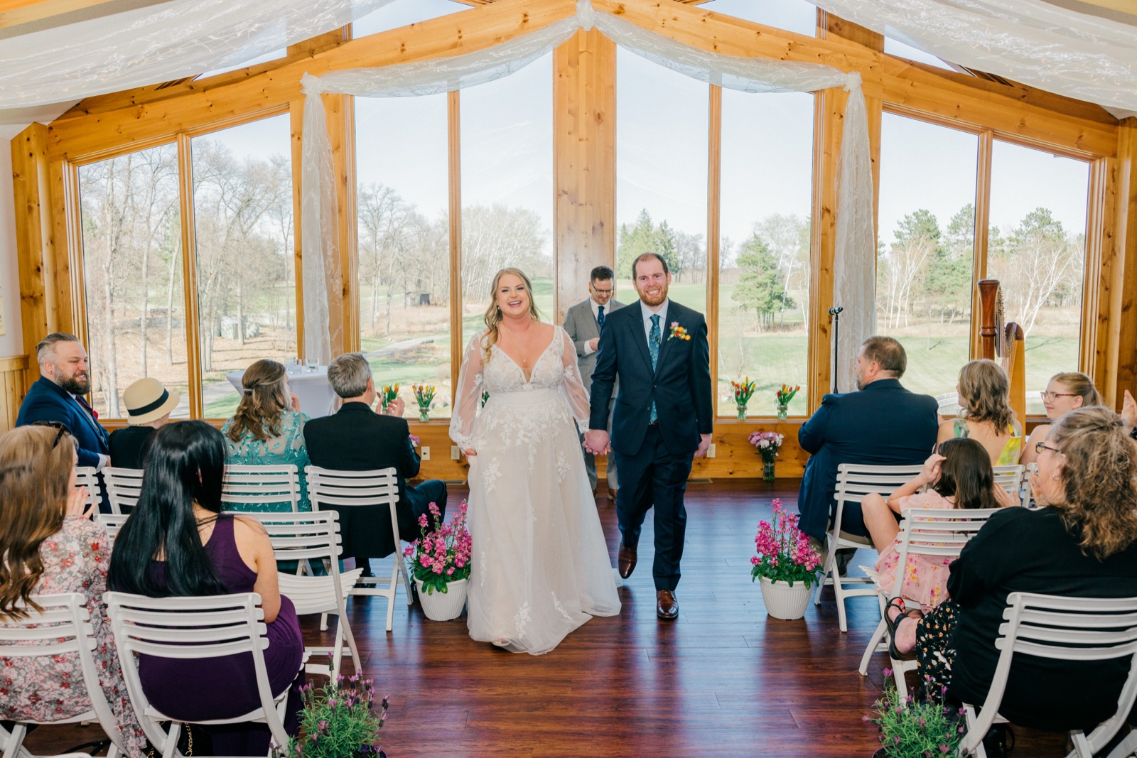The bride and groom hold hands and smile as they walk back down the aisle through the sunlit, wood-beamed Cragun's ceremony space — Tim Larsen Photography, Brainerd Lakes MN