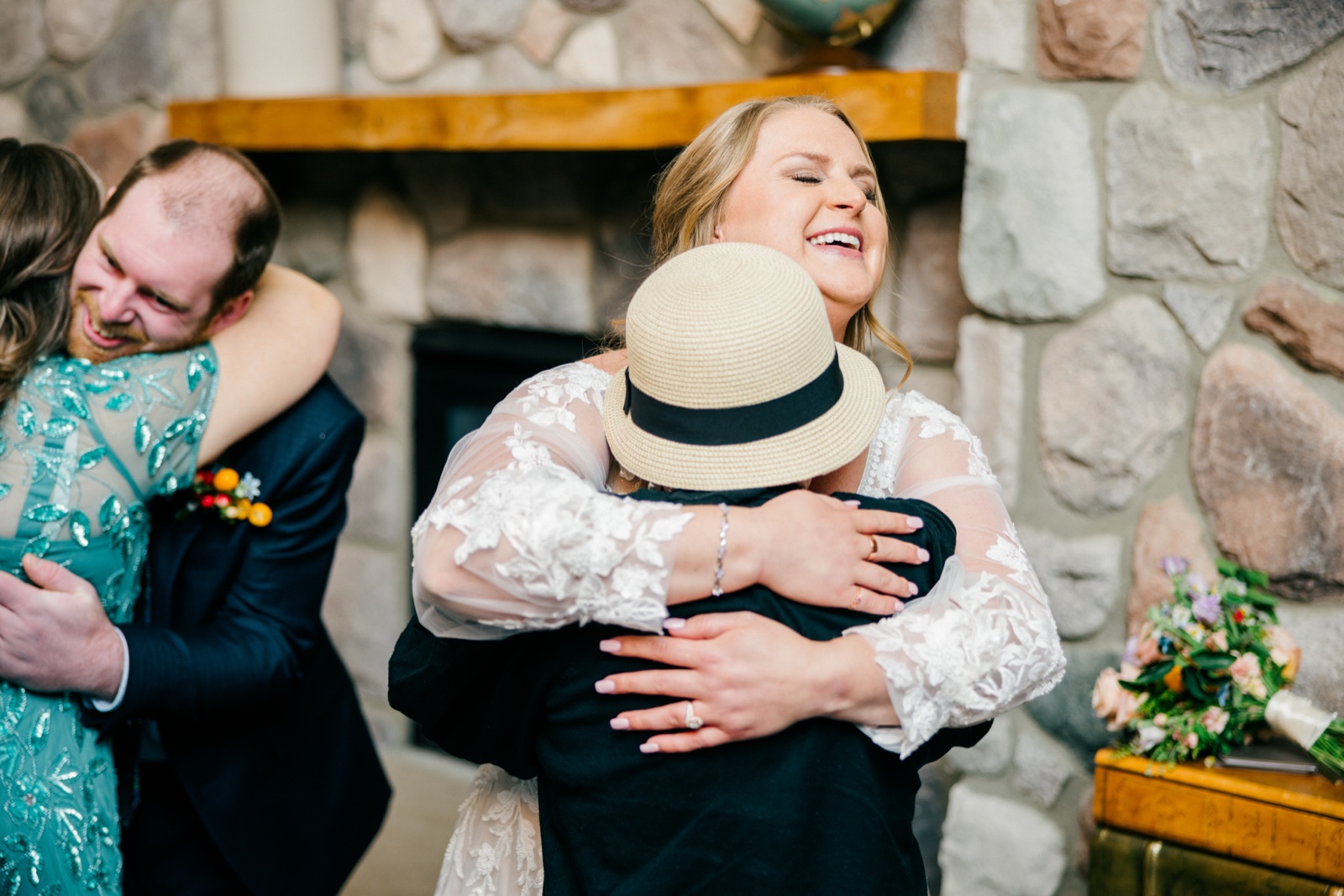 The bride laughs with eyes closed while embracing a guest in a straw hat in front of the stone fireplace at Cragun's — Tim Larsen Photography, Brainerd Lakes MN