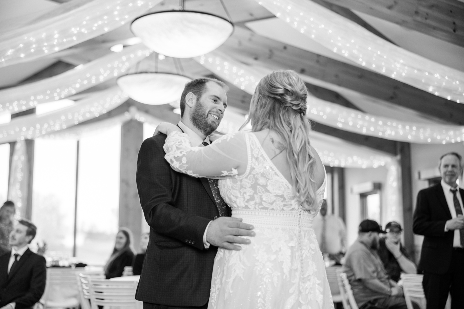 The groom smiles at his bride during their first dance under draped fabric and string lights at Cragun's Resort while seated guests watch — Tim Larsen Photography, Brainerd Lakes MN