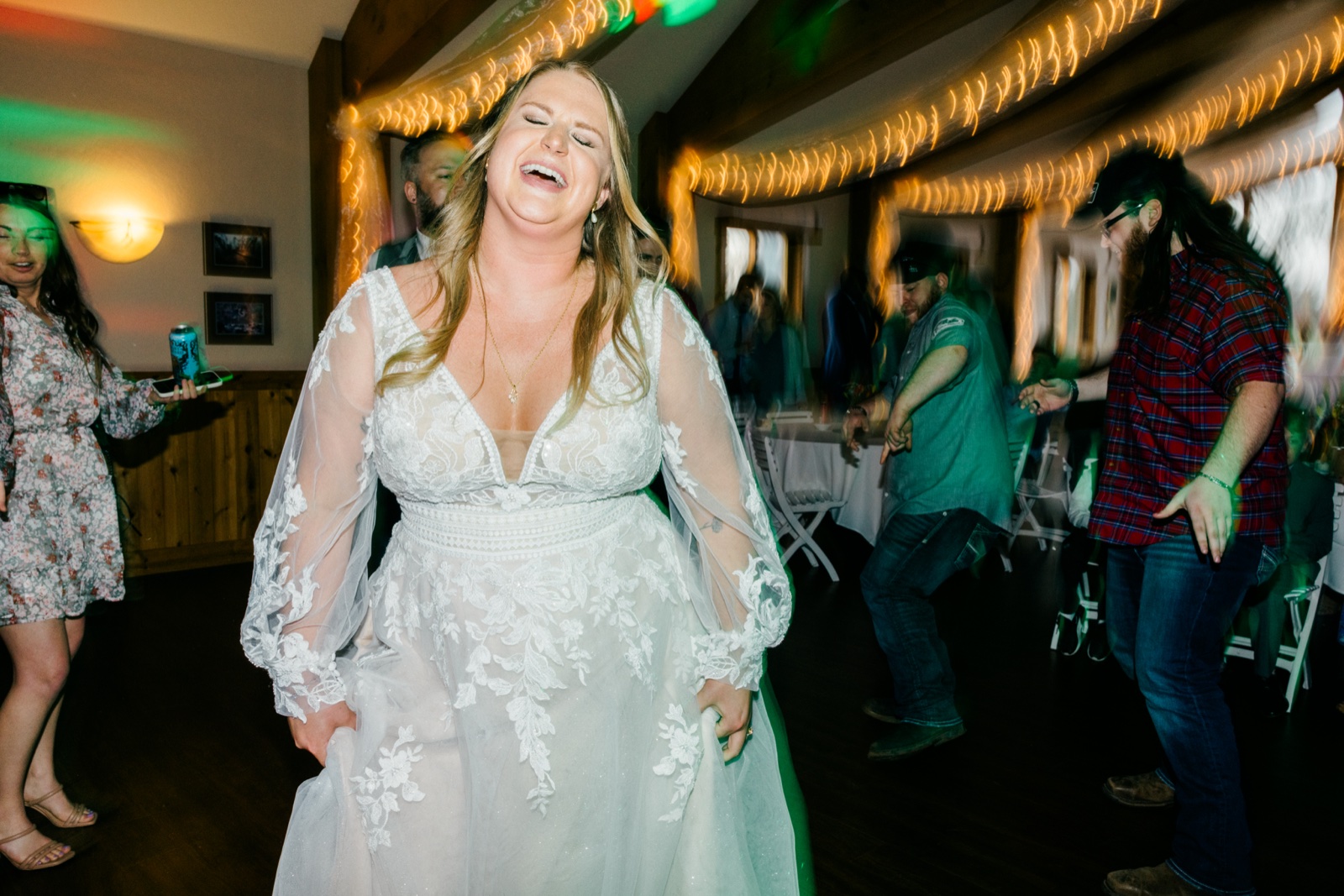 The bride throws her head back laughing on the dance floor while motion-blurred guests and string lights swirl around her at Cragun's — Tim Larsen Photography, Brainerd Lakes MN