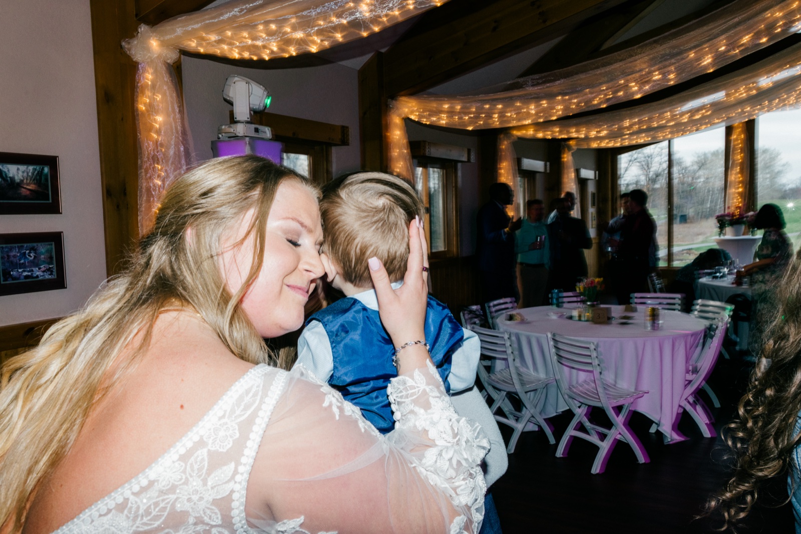 The bride closes her eyes and presses her forehead to a young boy's beneath the string-lit ceiling of the Cragun's reception — Tim Larsen Photography, Brainerd Lakes MN