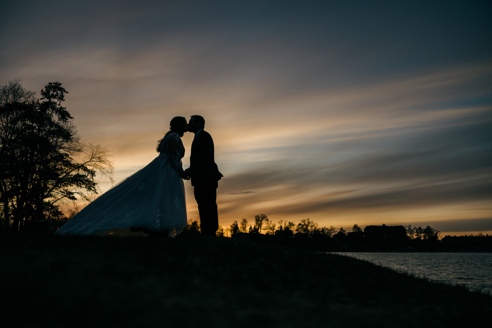 The bride and groom kiss in silhouette against an orange and blue dusk sky on the lakeshore at Cragun's Resort — Tim Larsen Photography, Brainerd Lakes MN