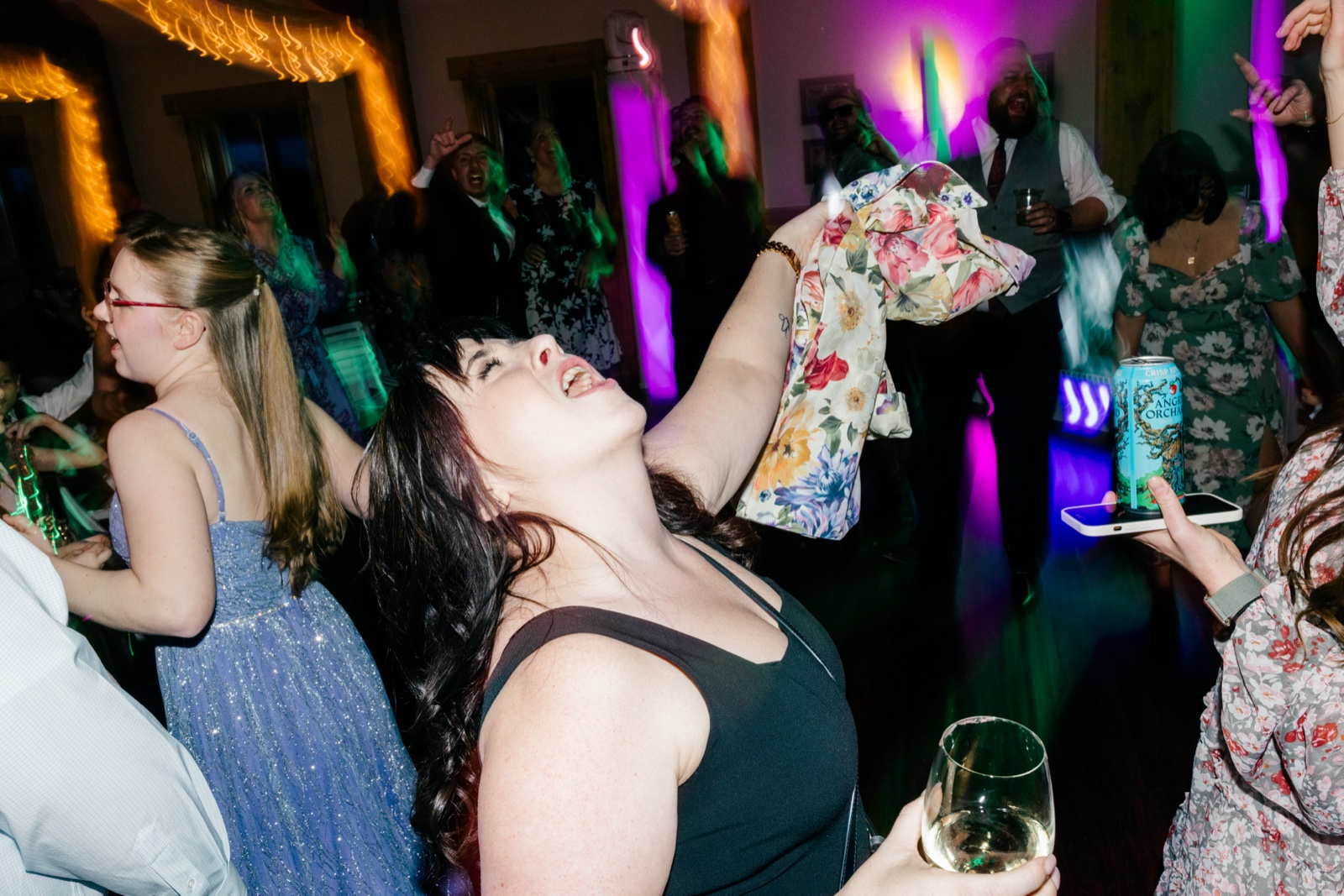 A guest in a black dress shouts mid-dance while another waves a floral jacket overhead amid purple stage lighting on the Cragun's dance floor — Tim Larsen Photography, Brainerd Lakes MN