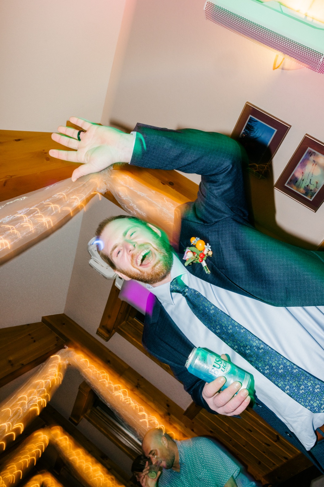 The groom throws his arms wide and laughs open-mouthed at the bar as a dragged-shutter flash streaks the warm reception lights behind him — Tim Larsen Photography, Brainerd Lakes MN